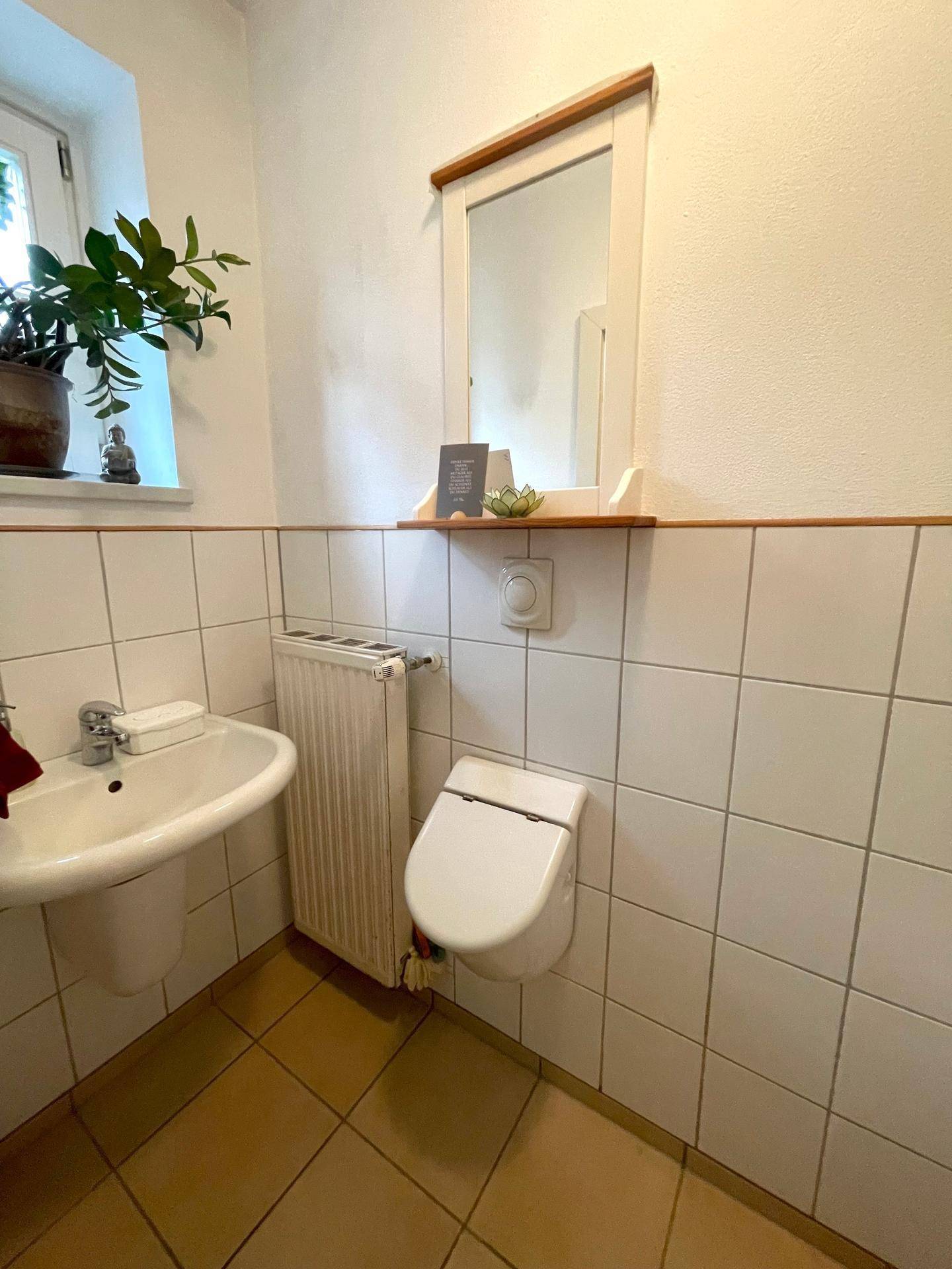 Helles Gäste-WC mit Fliesenboden, wandhängendem WC und Fenster.