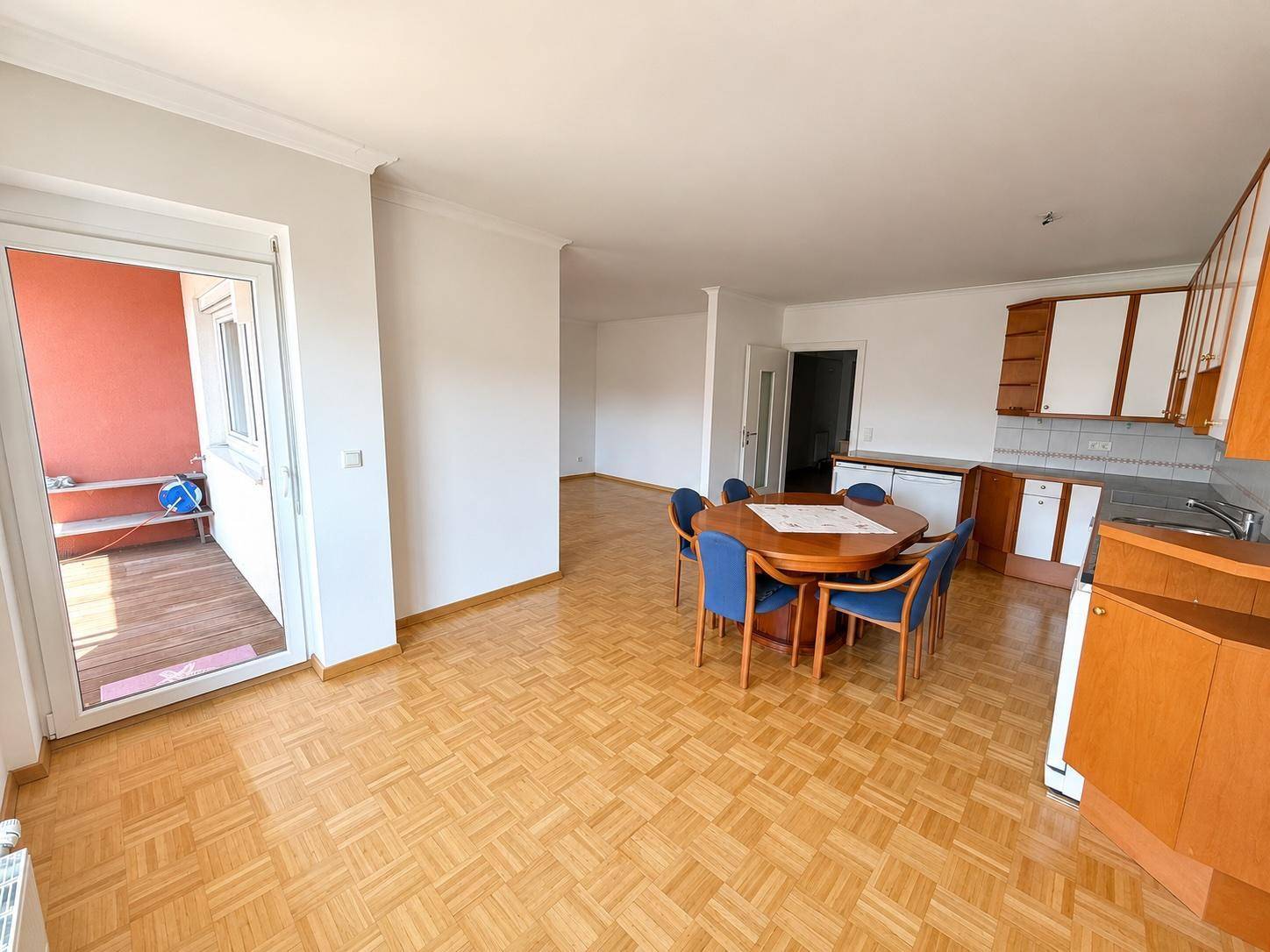 Heller Wohn-Essbereich mit Zugang zum Balkon, ausgestattet mit einer Einbauküche und Parkettboden.