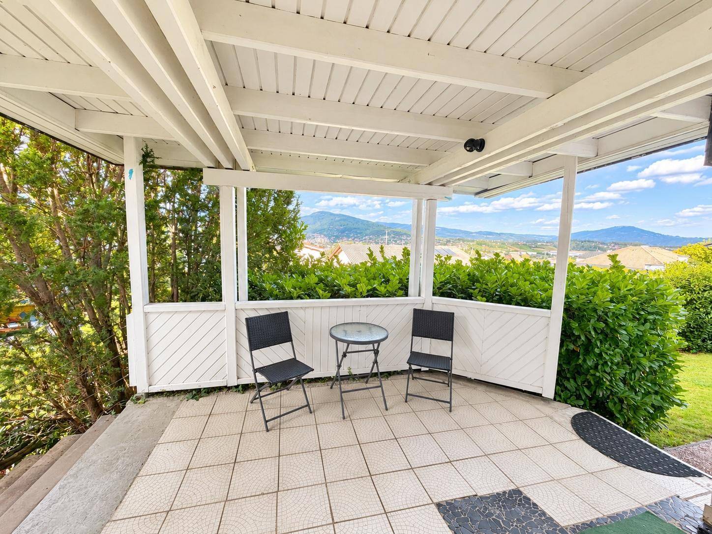 Überdachte Terrasse mit Fliesenboden und einem weiten Panoramablick auf die Berge und das Tal.