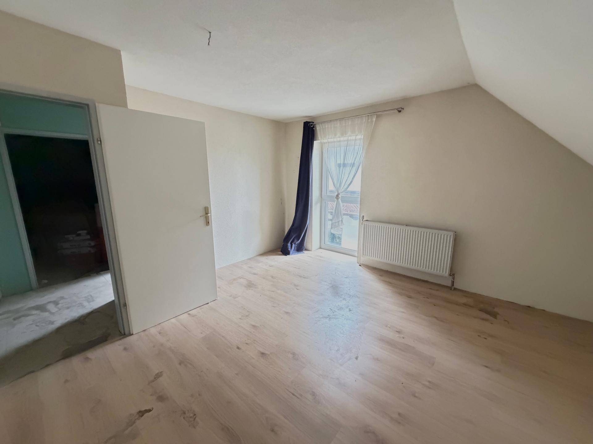 Helles Dachgeschosszimmer mit Holzboden, schräger Decke und Zugang zum Balkon, viel Tageslicht.