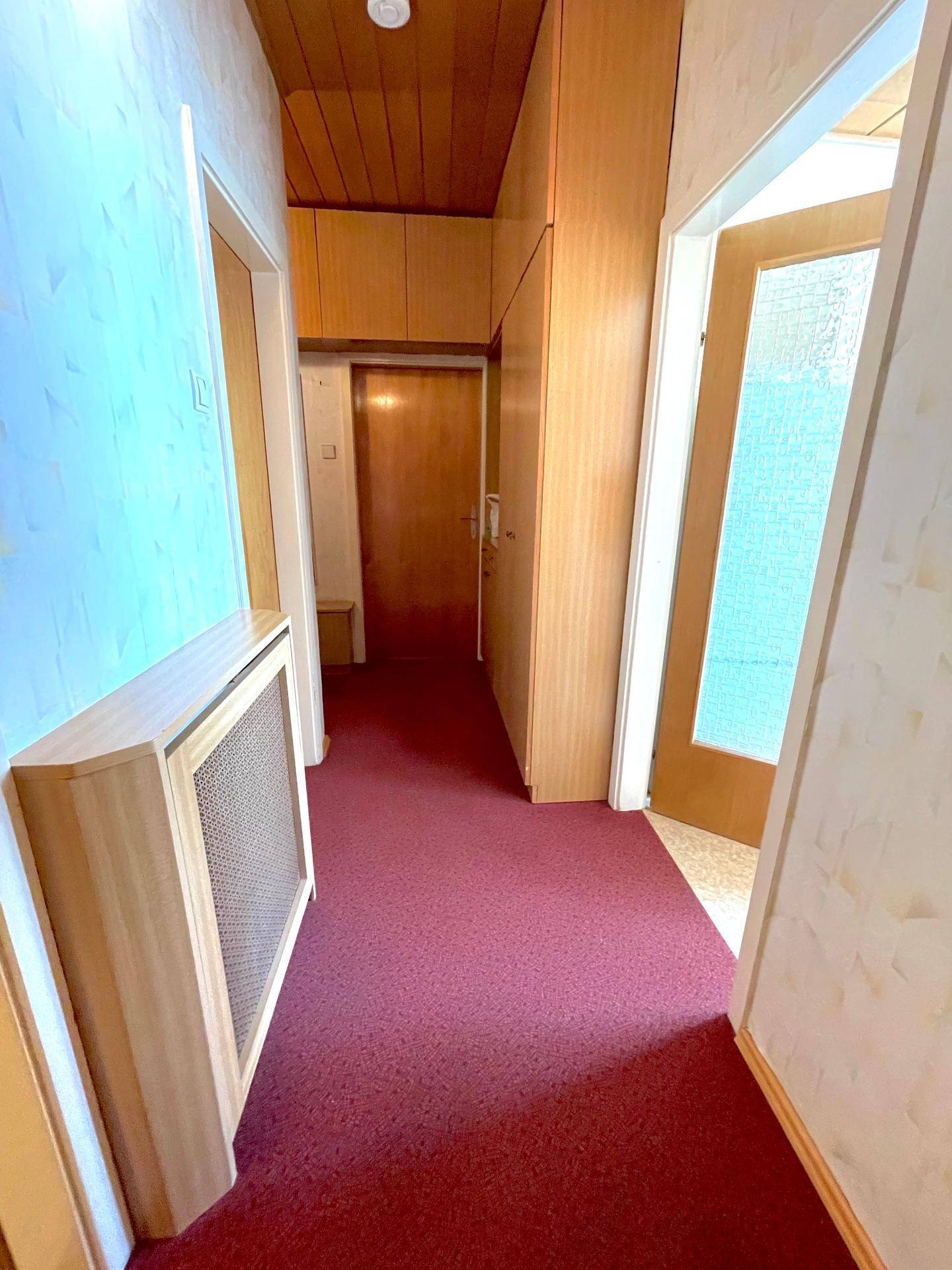 Langer Flur mit Teppichboden, Holzverkleidung und Zugang zu mehreren Zimmern.