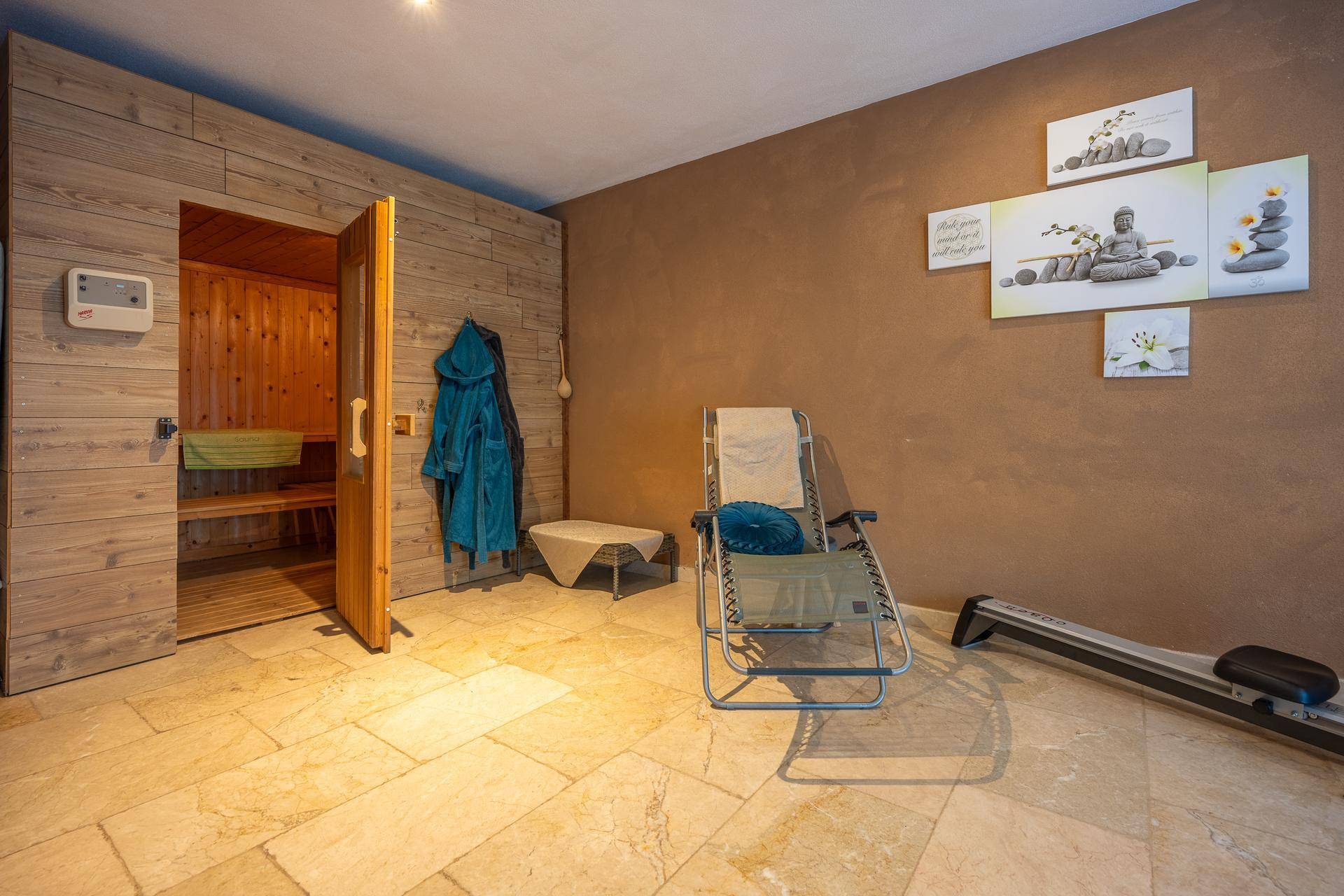 Entspannungsbereich mit Sauna, Liegestuhl und Trainingsgerät auf hellem Fliesenboden.