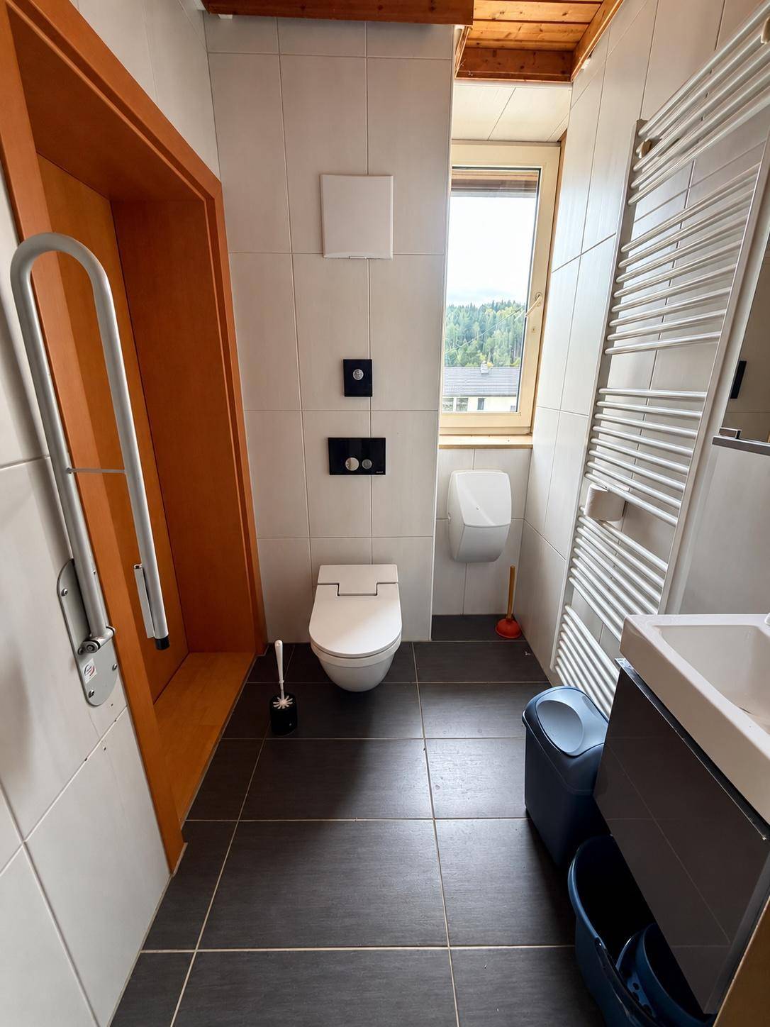 Modernes Badezimmer mit WC, Urinal, Waschbecken und Haltegriffen.