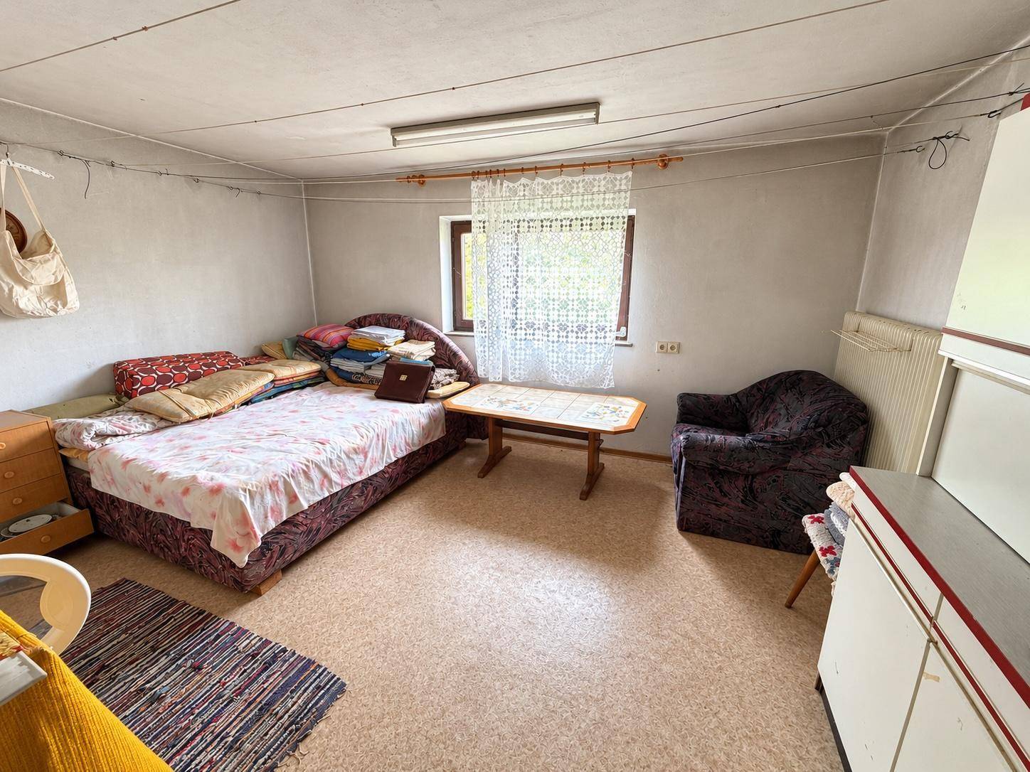 Einfacher Kellerraum mit Bett, Teppichboden und Fenster.