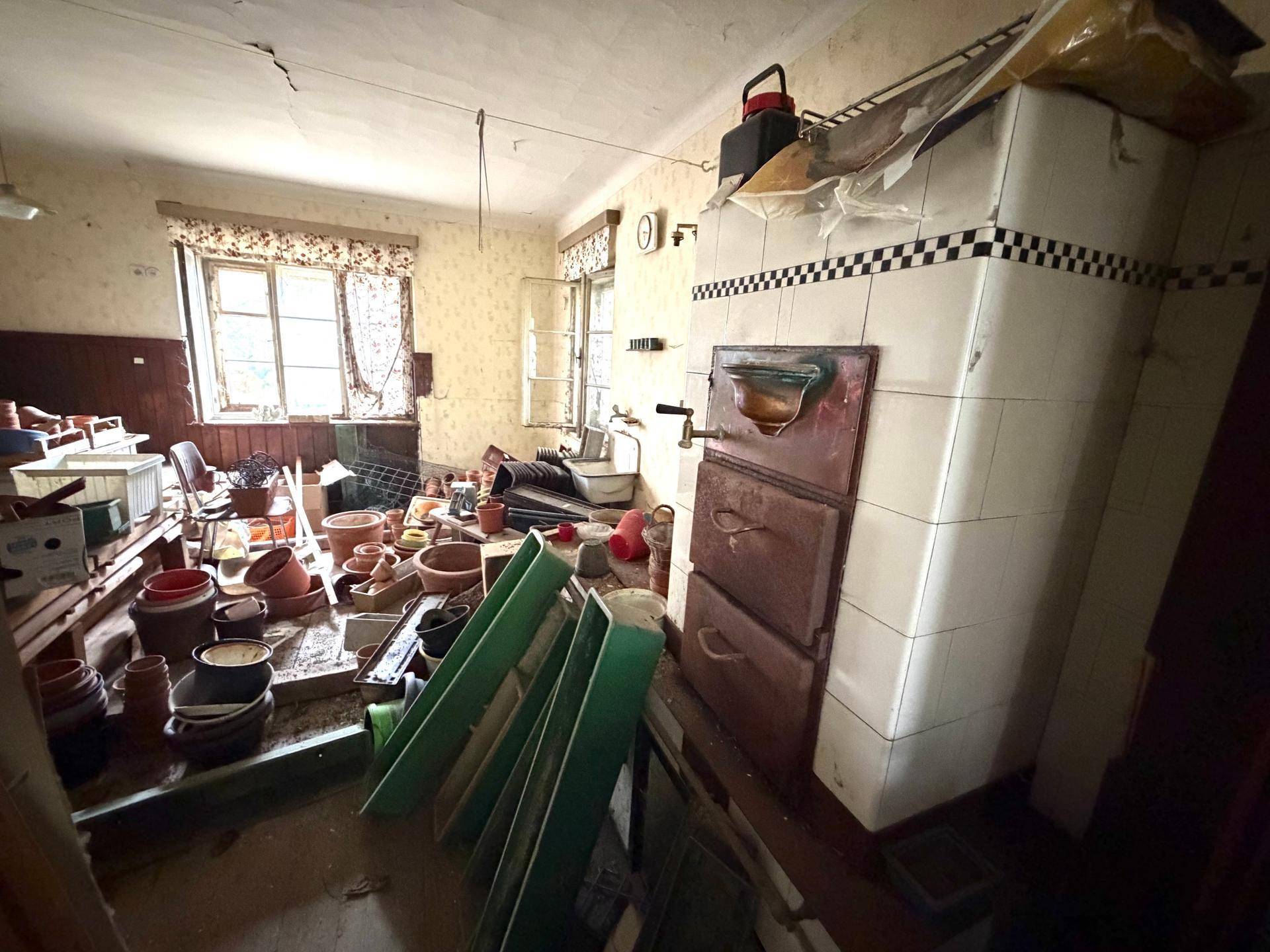 Alte Küche mit traditionellem Kachelofen, Fenster und viel Stauraum für Utensilien.