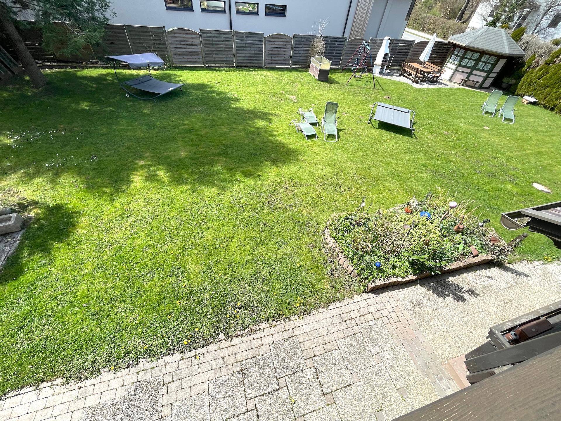 Ein großer, gepflegter Garten mit Rasenfläche, Blumenbeeten und Spielgeräten.