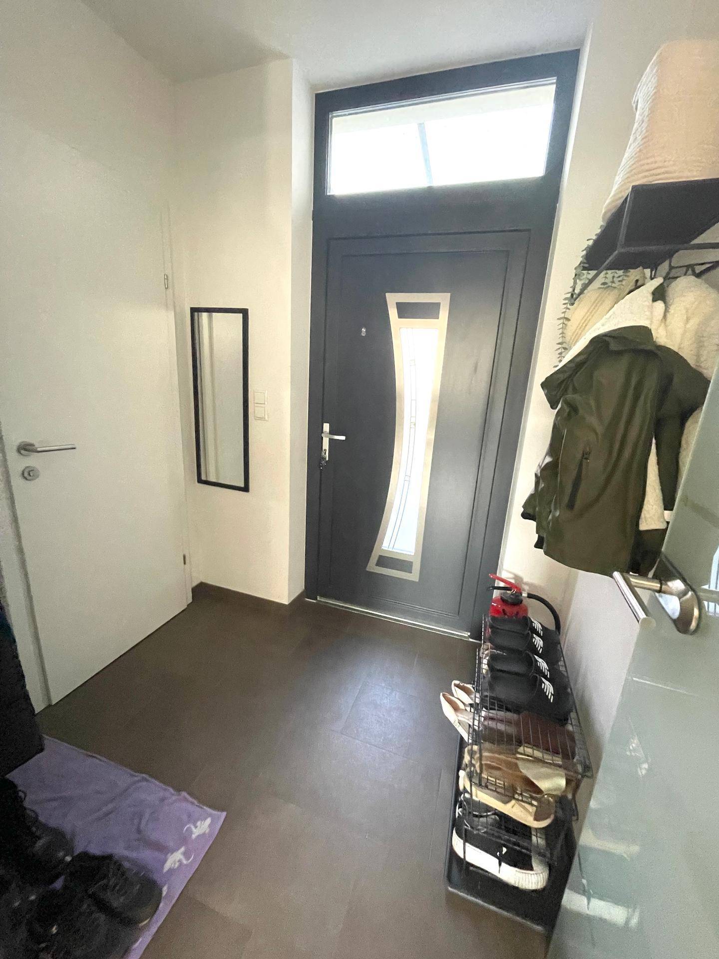Eingangsbereich mit dunkler Eingangstür, Schuhregal und Garderobe.