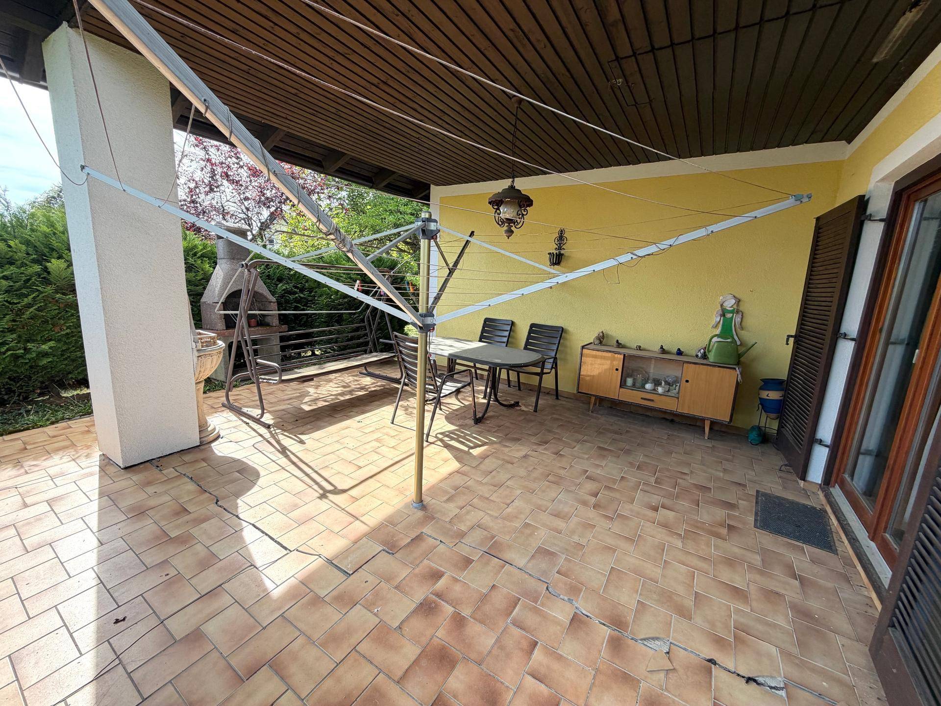 Überdachte Terrasse mit Fliesenboden, Grillplatz und Wäschespinne im Freien.