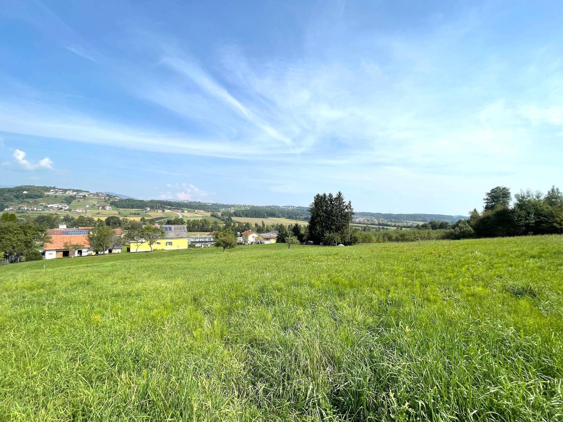 Offenes grünes Feld mit Panoramablick auf die hügelige Landschaft und Siedlung.