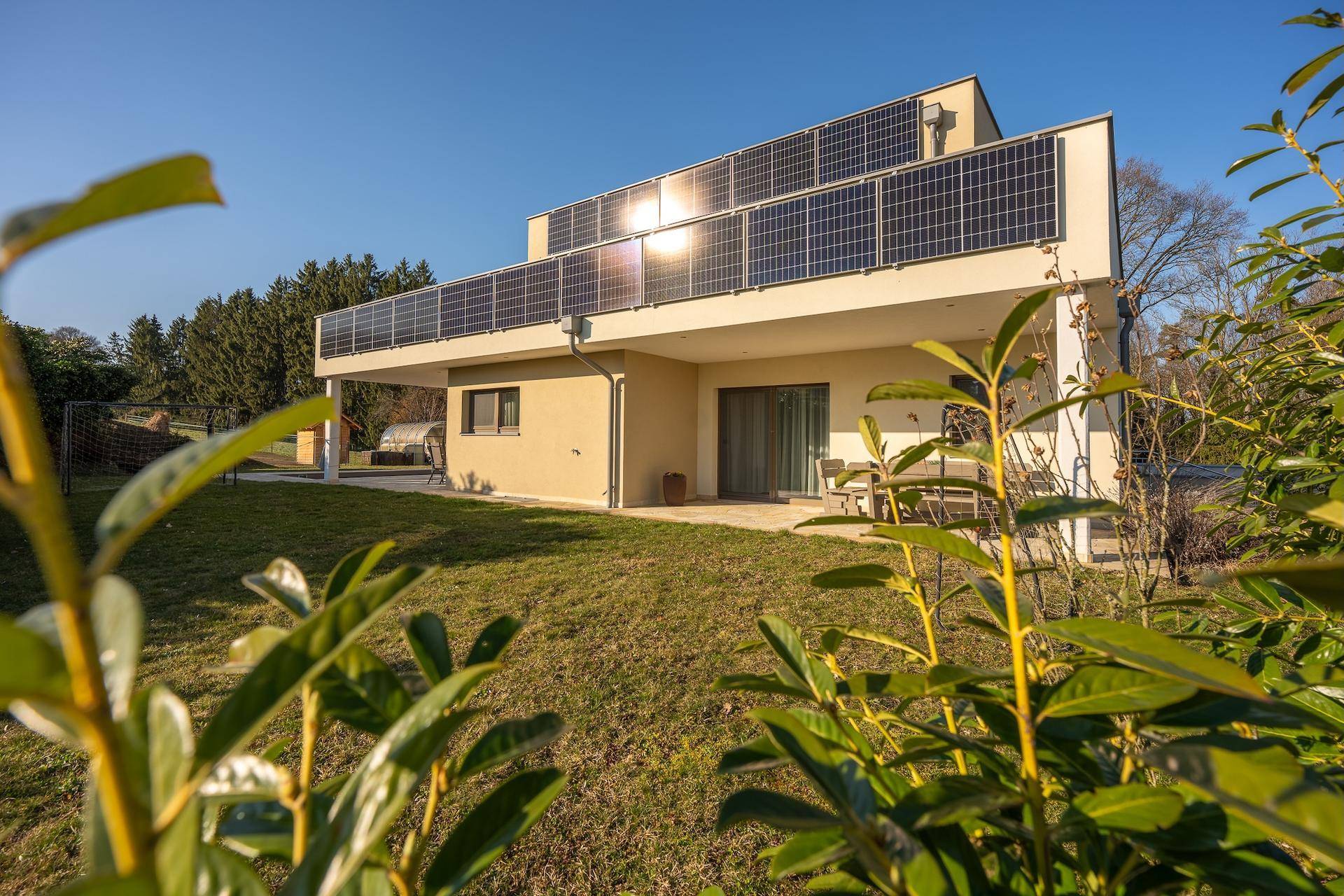 Modernes Wohnhaus mit Photovoltaikanlage und gepflegtem Garten unter strahlendem Himmel.
