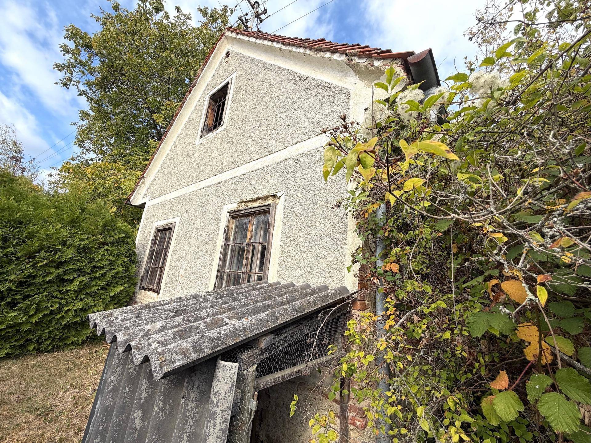 Seitenansicht des Hauses mit Anbau, alten Fenstern und verputzter Fassade.