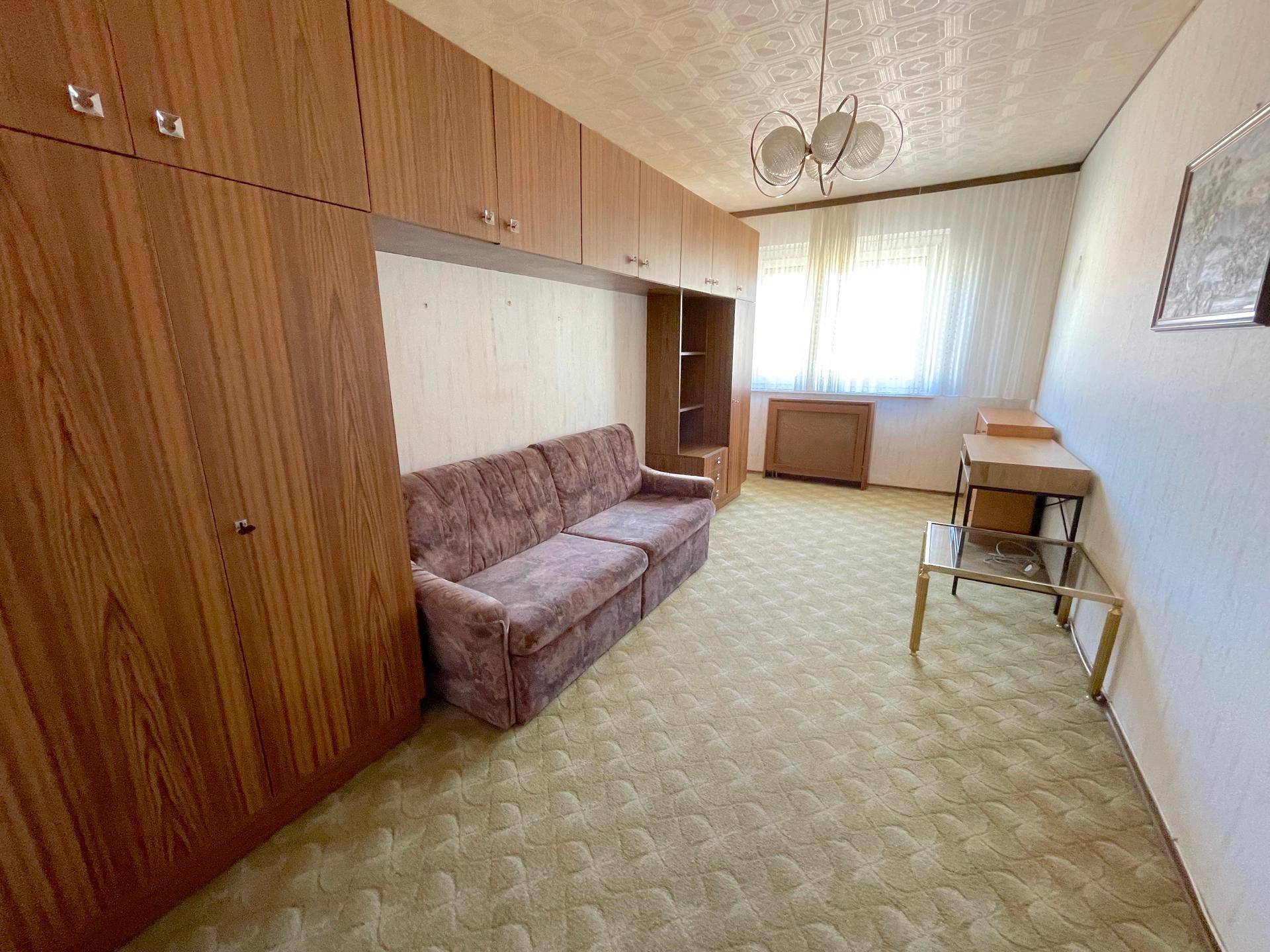 Wohnzimmer mit Sofa, Schrankwand und Teppichboden, typisch für ältere Einrichtung.