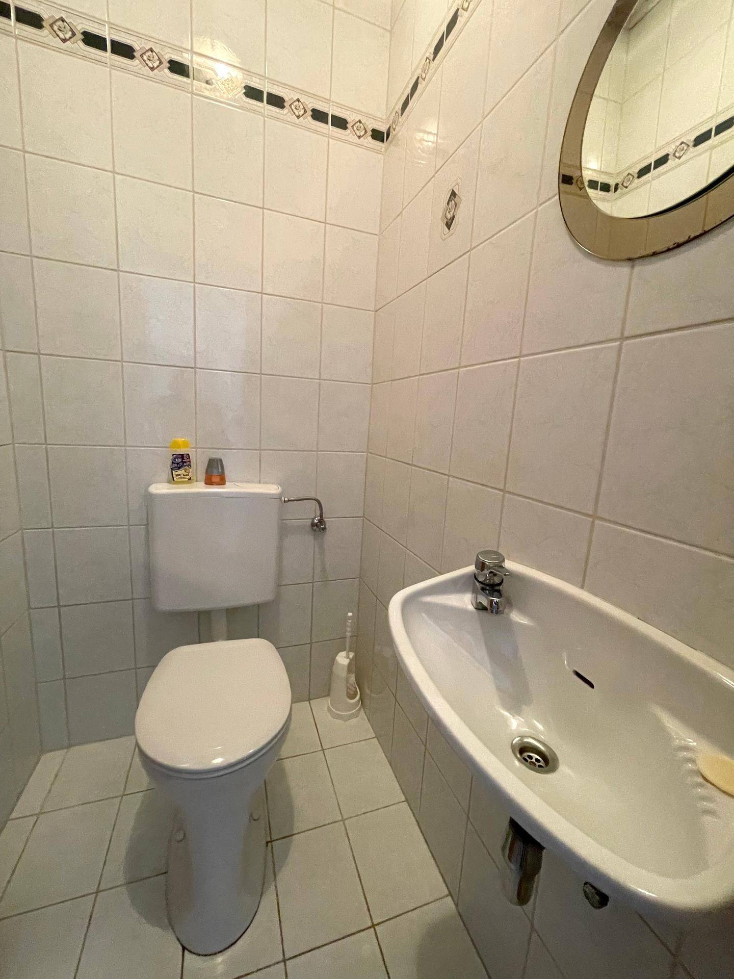 Kleines Gäste-WC mit wandmontierter Toilette, Waschbecken und weißen Fliesen.