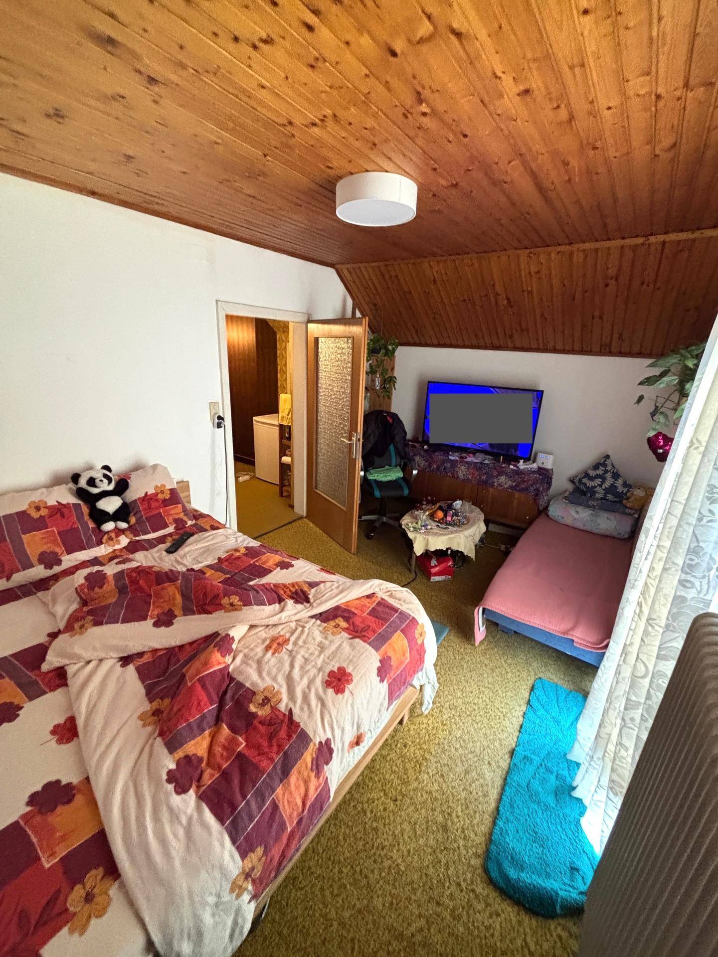 Schlafzimmer mit Holzdecke, Doppelbett und Fernseher, hell durch Fenster.