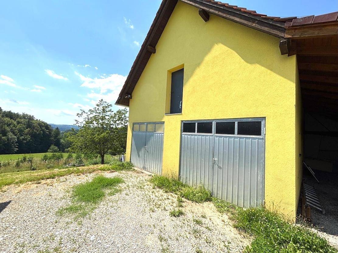 Gelbes Gebäude mit zwei Metallgaragentoren, umgeben von grüner Landschaft.