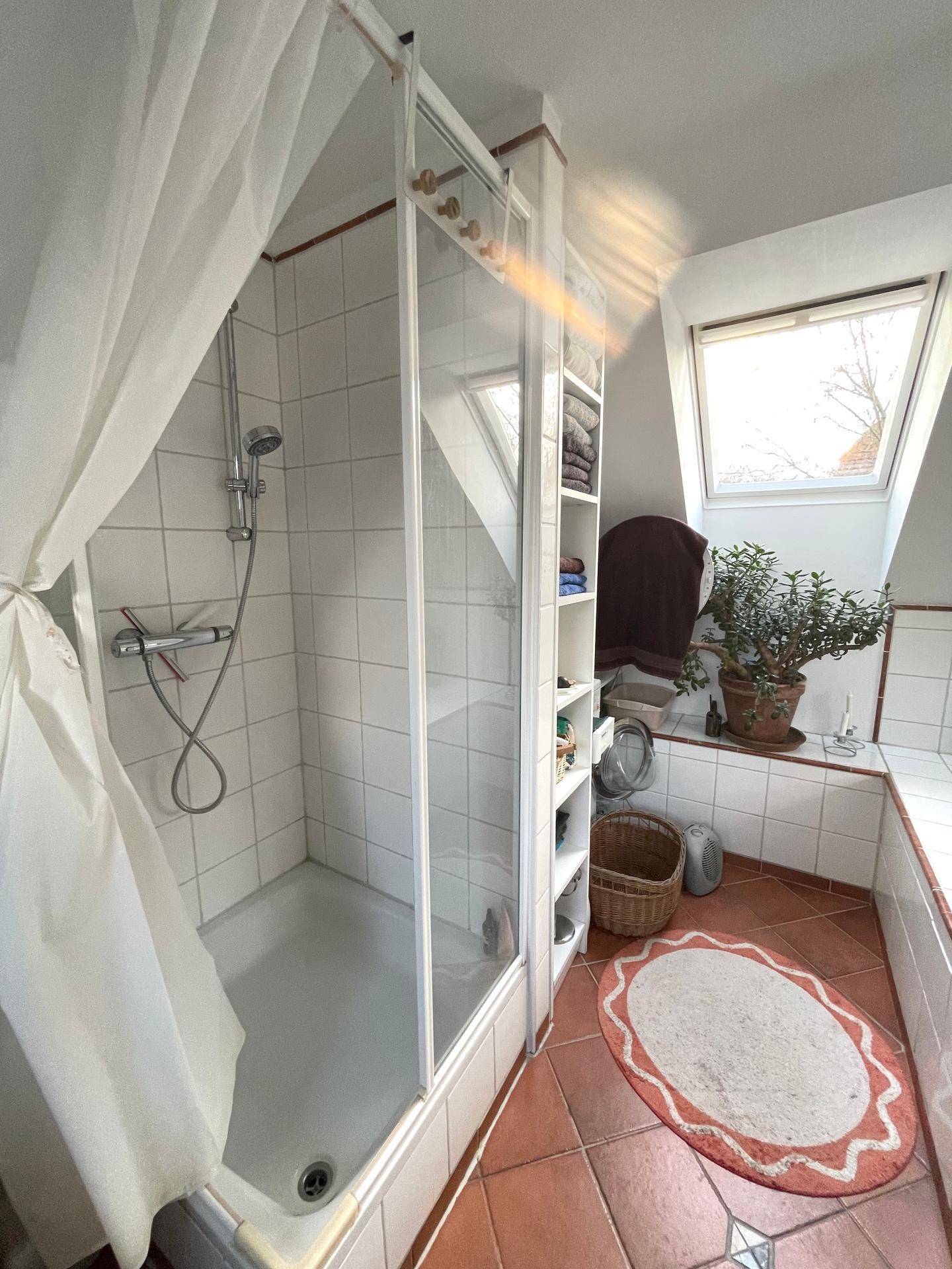 Badezimmer im Dachgeschoss mit Dusche, Fliesenboden und Dachfenster.