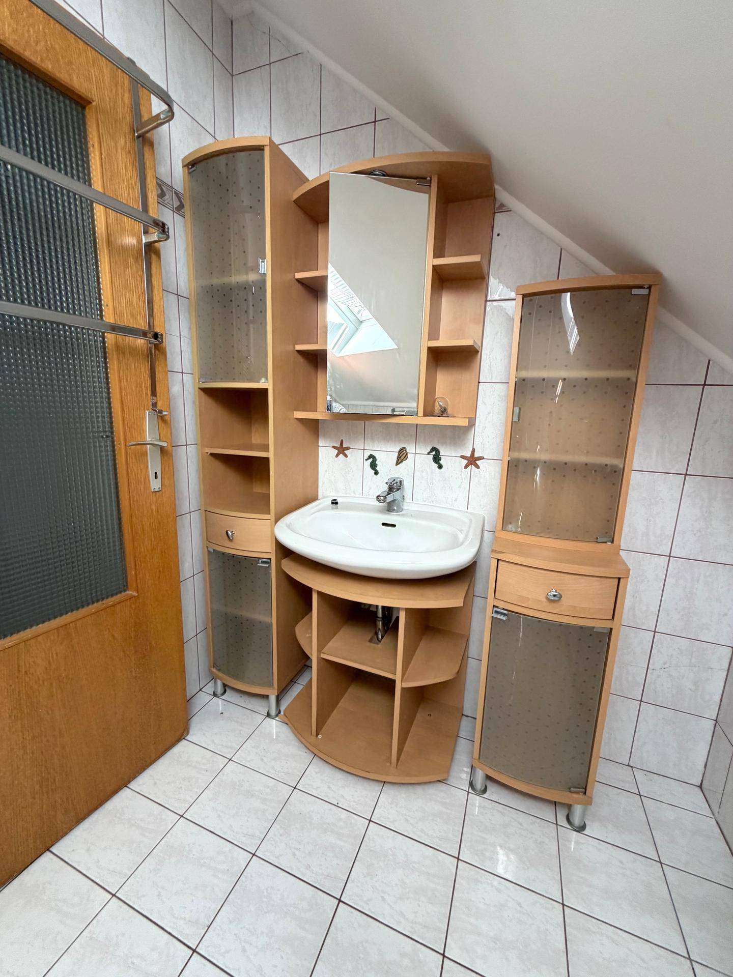 Badezimmer mit Holzwaschtisch, Spiegel und Stauraum unter dem Dachschrägen.