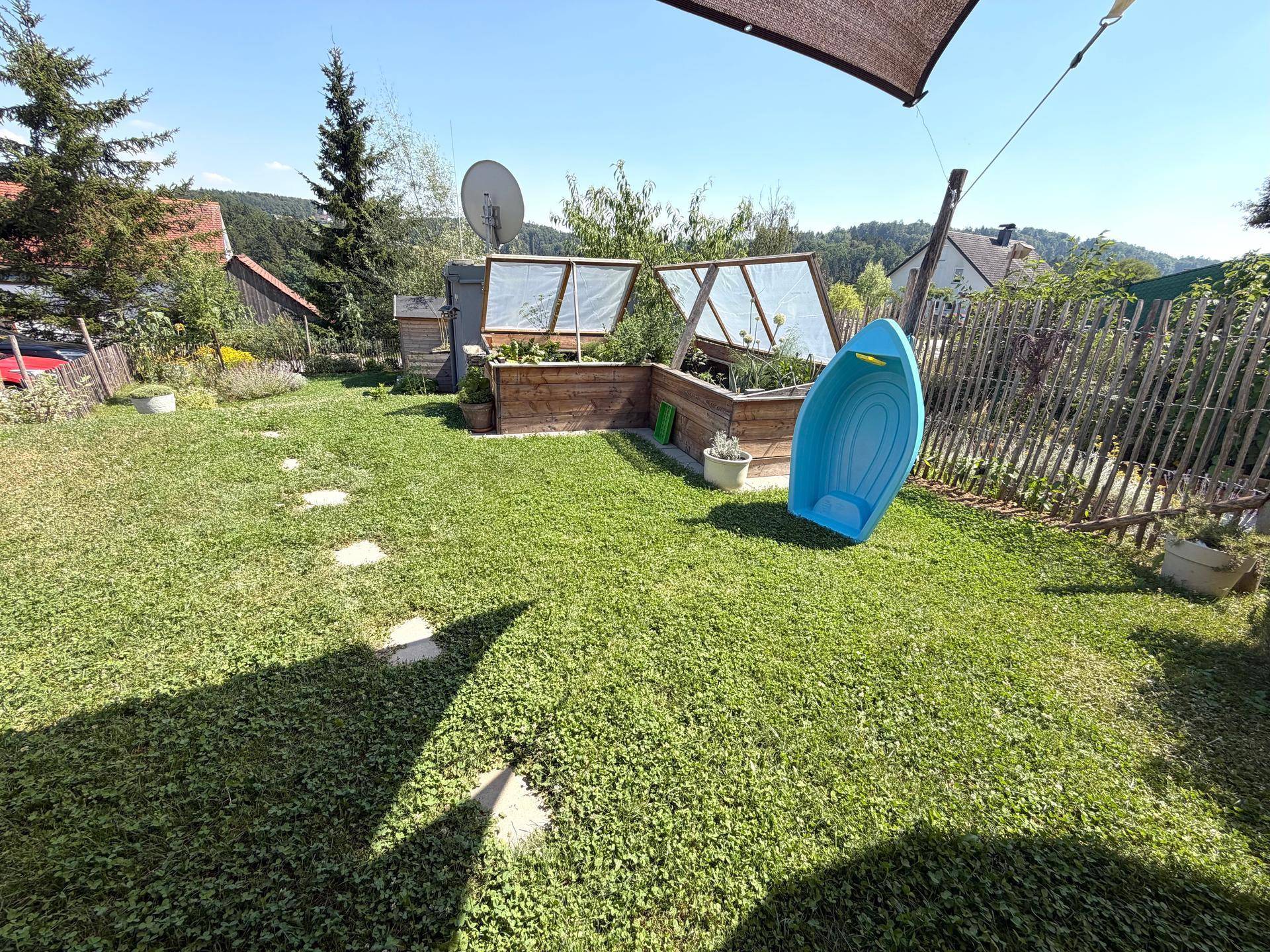 Sonniger Garten mit Rasen, Trittsteinen und Hochbeeten, ideal für Entspannung.