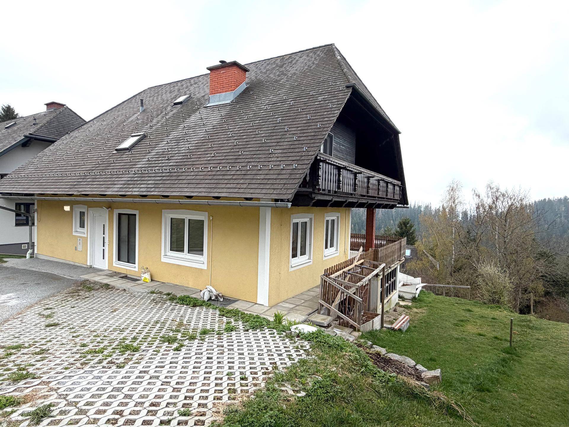 Seitenansicht des Hauses mit gelber Fassade, Satteldach und Zufahrt zum Grundstück.