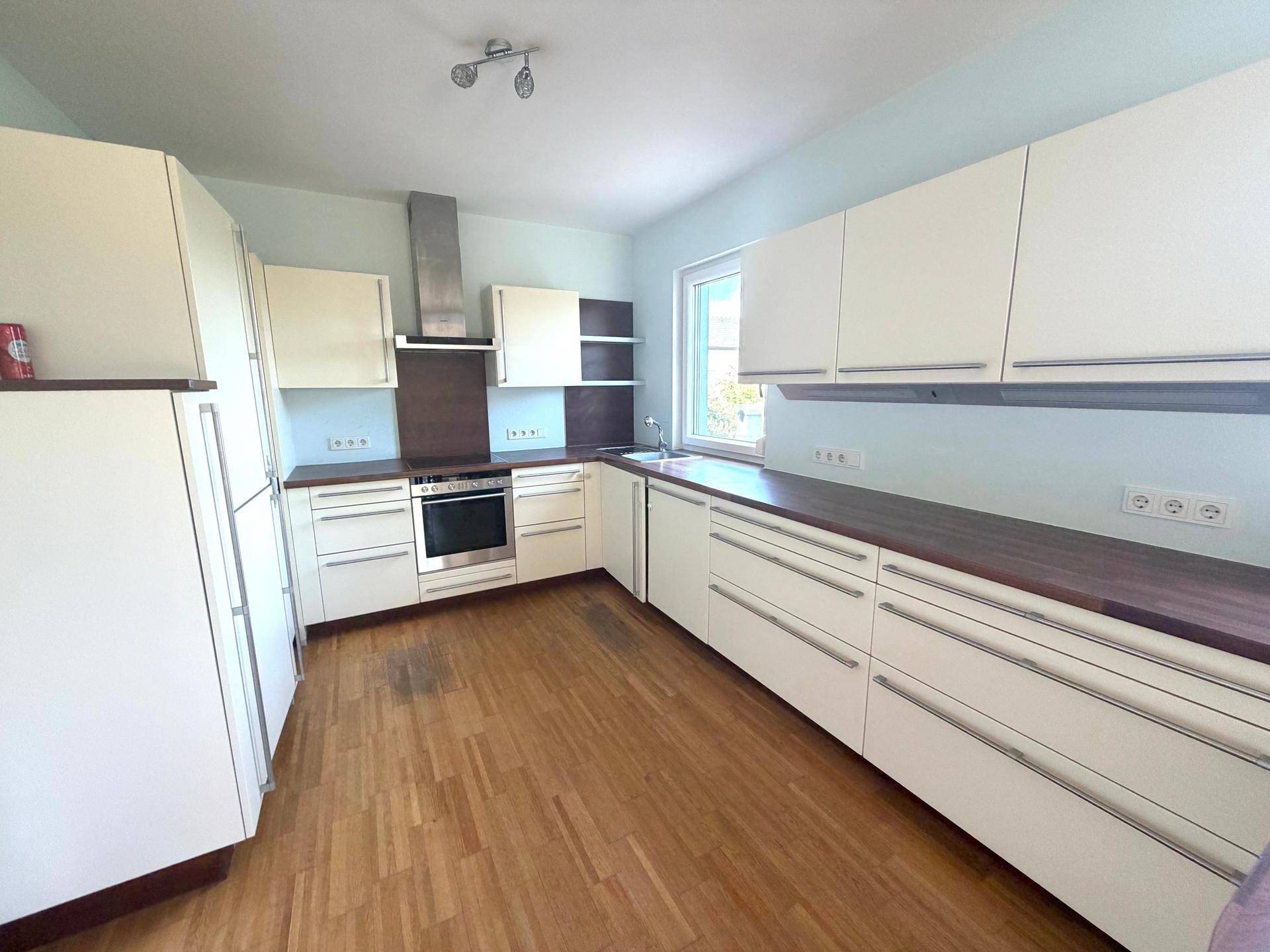 Moderne Einbauküche mit hellen Schränken, Holztheke und Holzboden in gutem Zustand.
