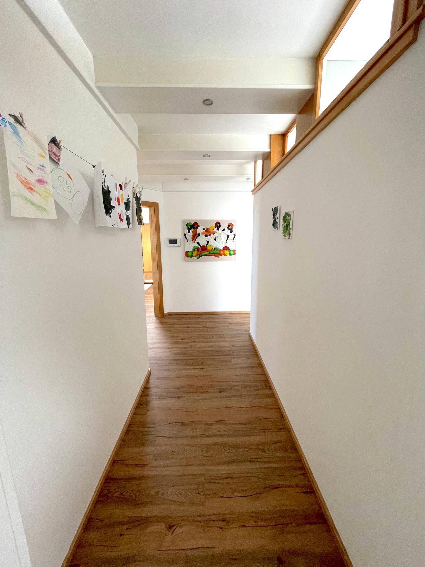 Heller Flur mit Holzfußboden, weißen Wänden und dekorativen Fenstern nahe der Decke.