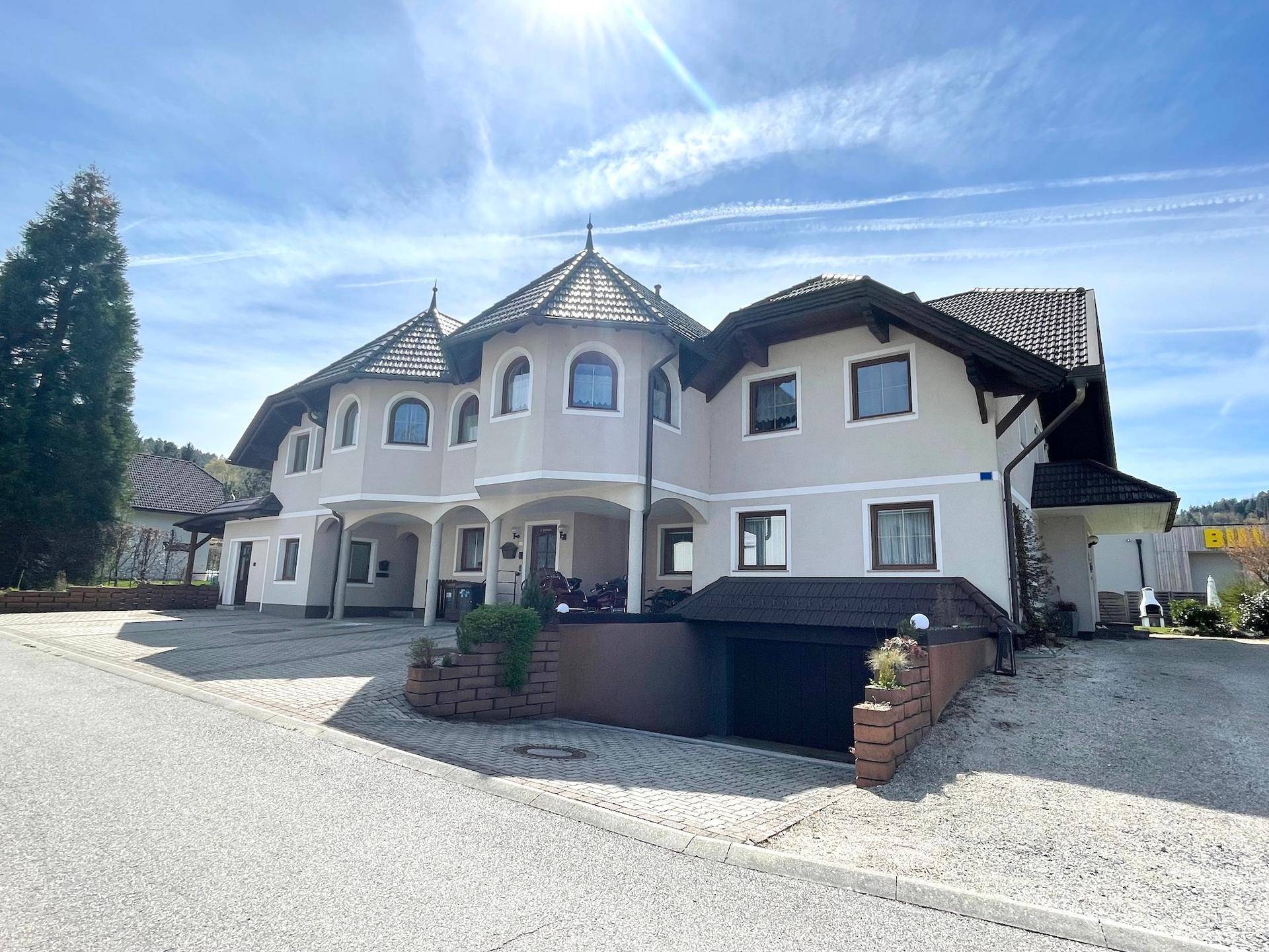 Die Vorderseite des Hauses mit markanten Türmchen und gepflasterter Auffahrt.