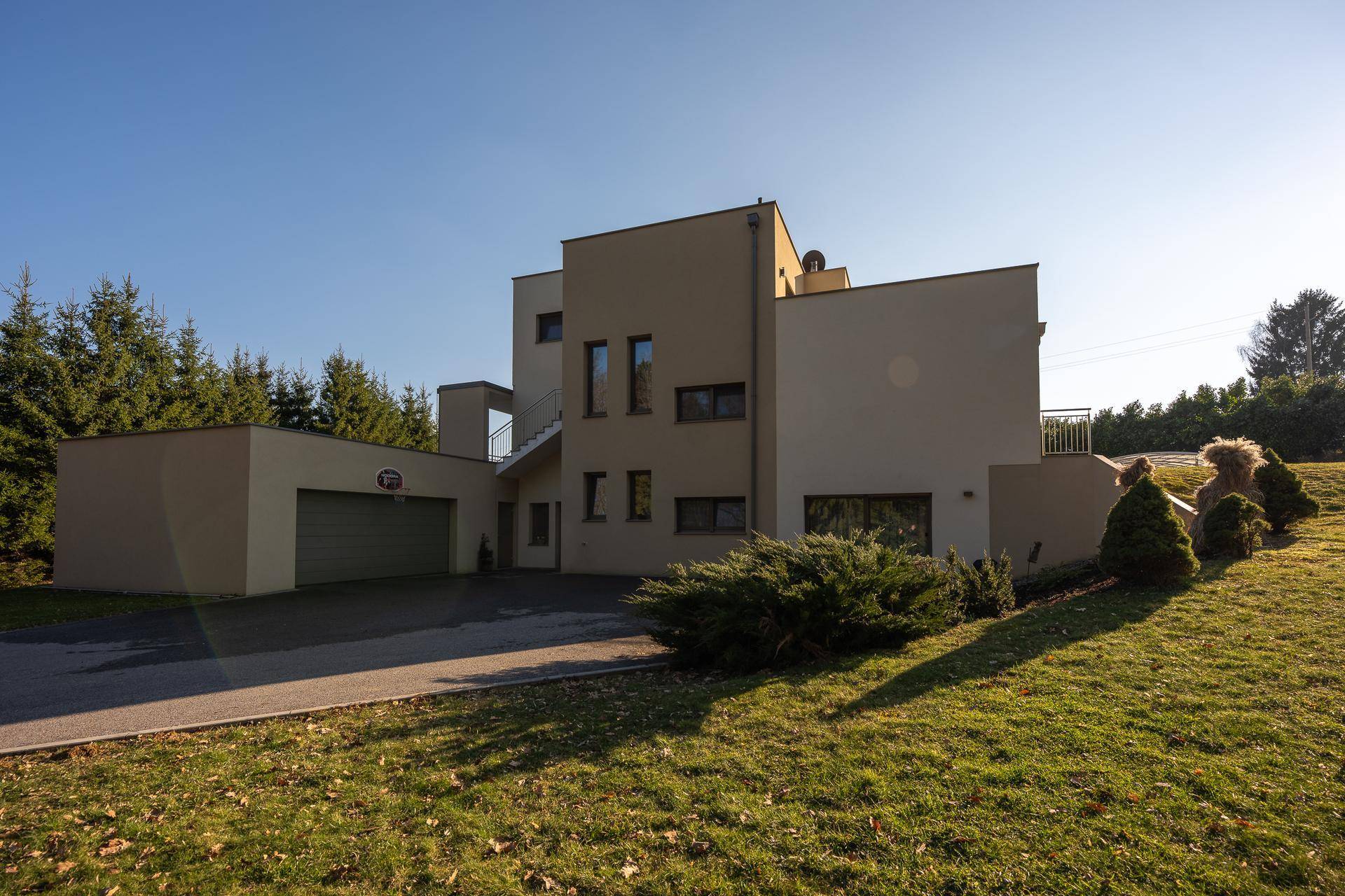 Moderne Villa mit Garage, Auffahrt und gepflegtem Gartenbereich unter blauem Himmel.