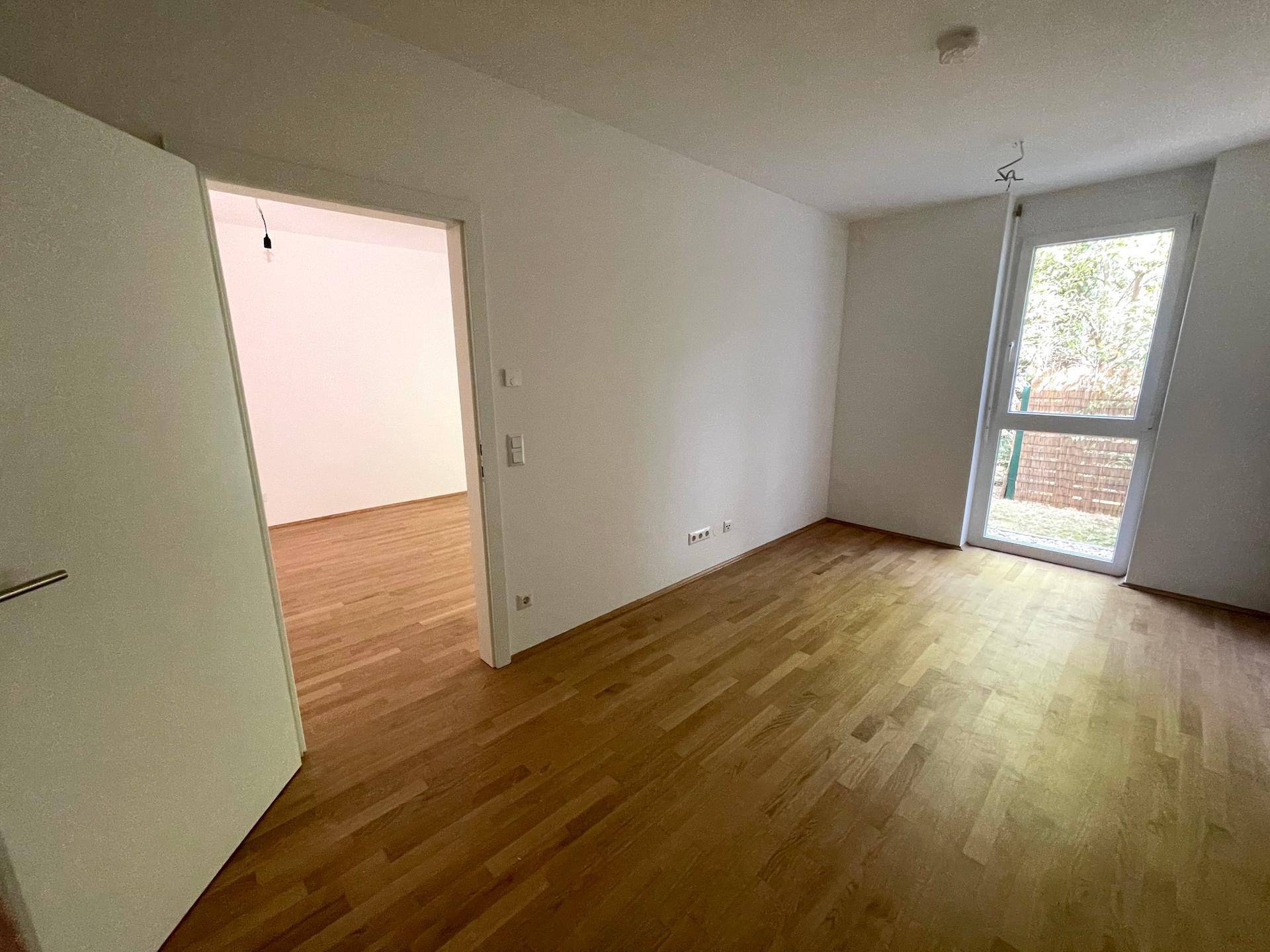 Helles Schlafzimmer mit Holzboden und Zugang zu einem kleinen Außenbereich durch eine hohe Tür.
