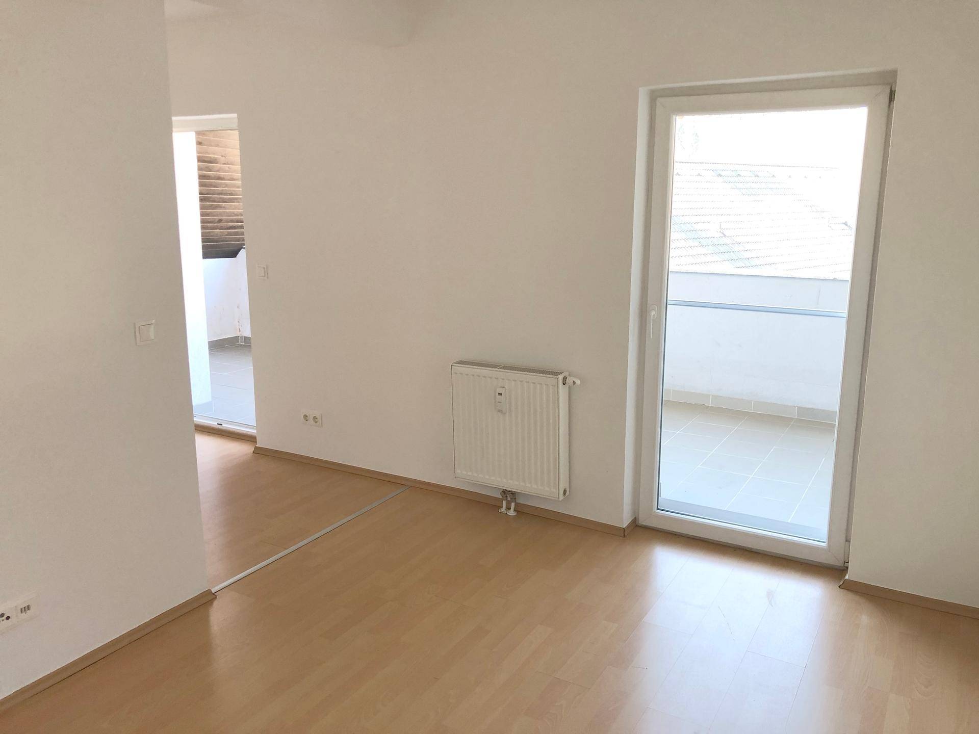 Lichtdurchfluteter Raum mit Laminatboden und Zugang zu einem weiteren Balkon.