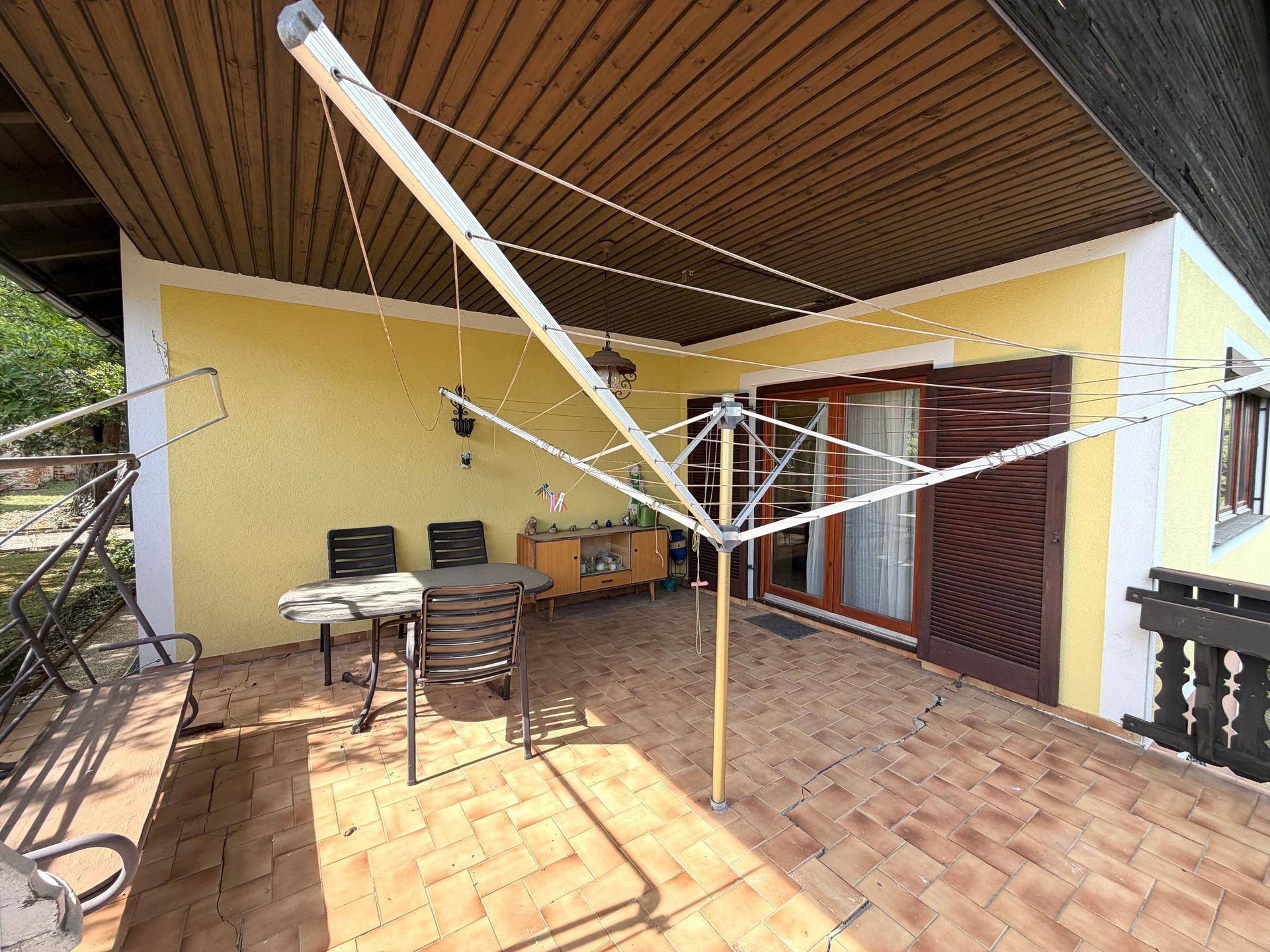 Überdachte Terrasse mit Fliesenboden, Sitzgelegenheiten und Zugang zum Haus.