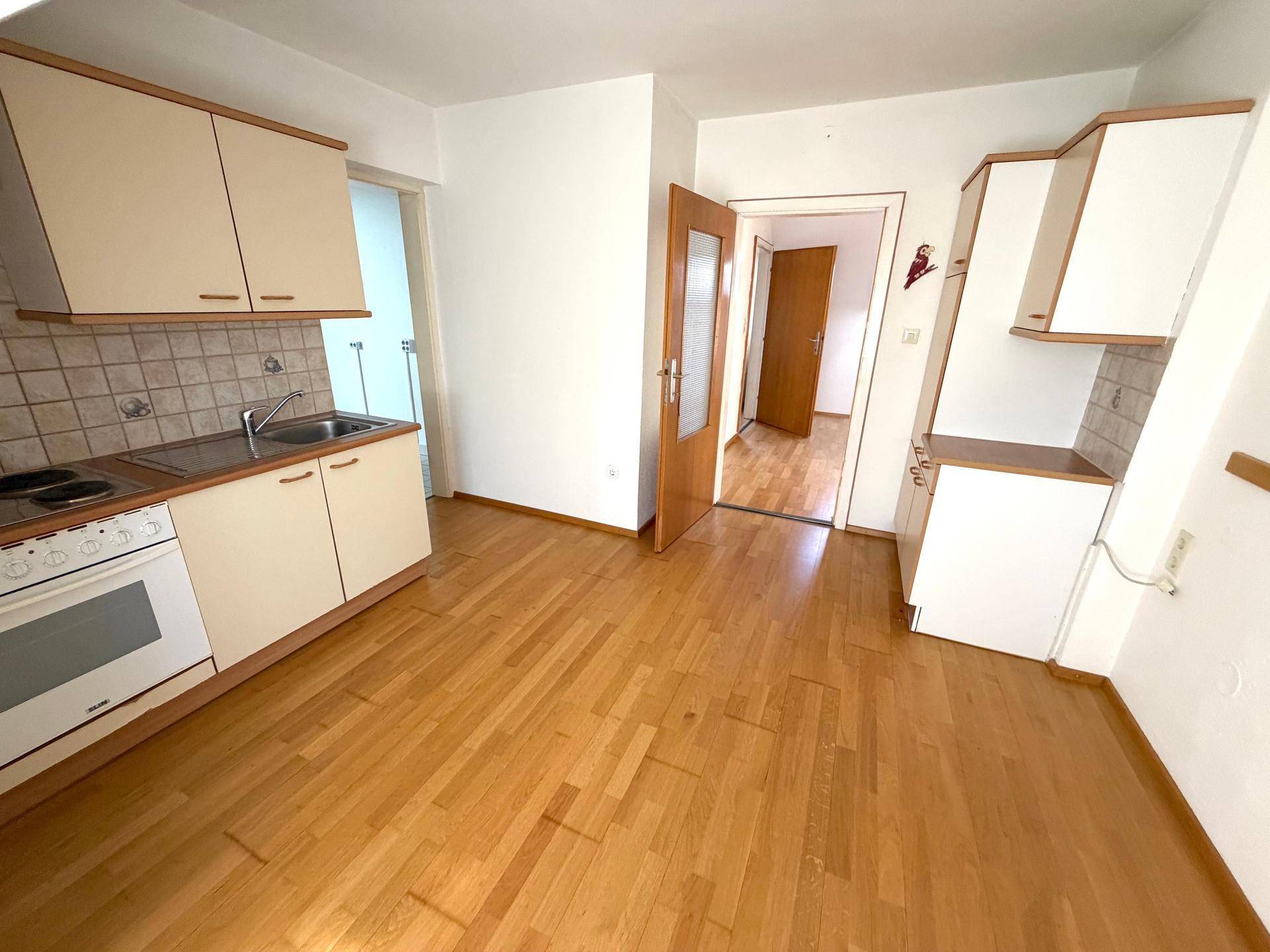 Kleine Küche mit Einbaugeräten, Holzoptik-Boden und Zugang zu weiteren Räumen.