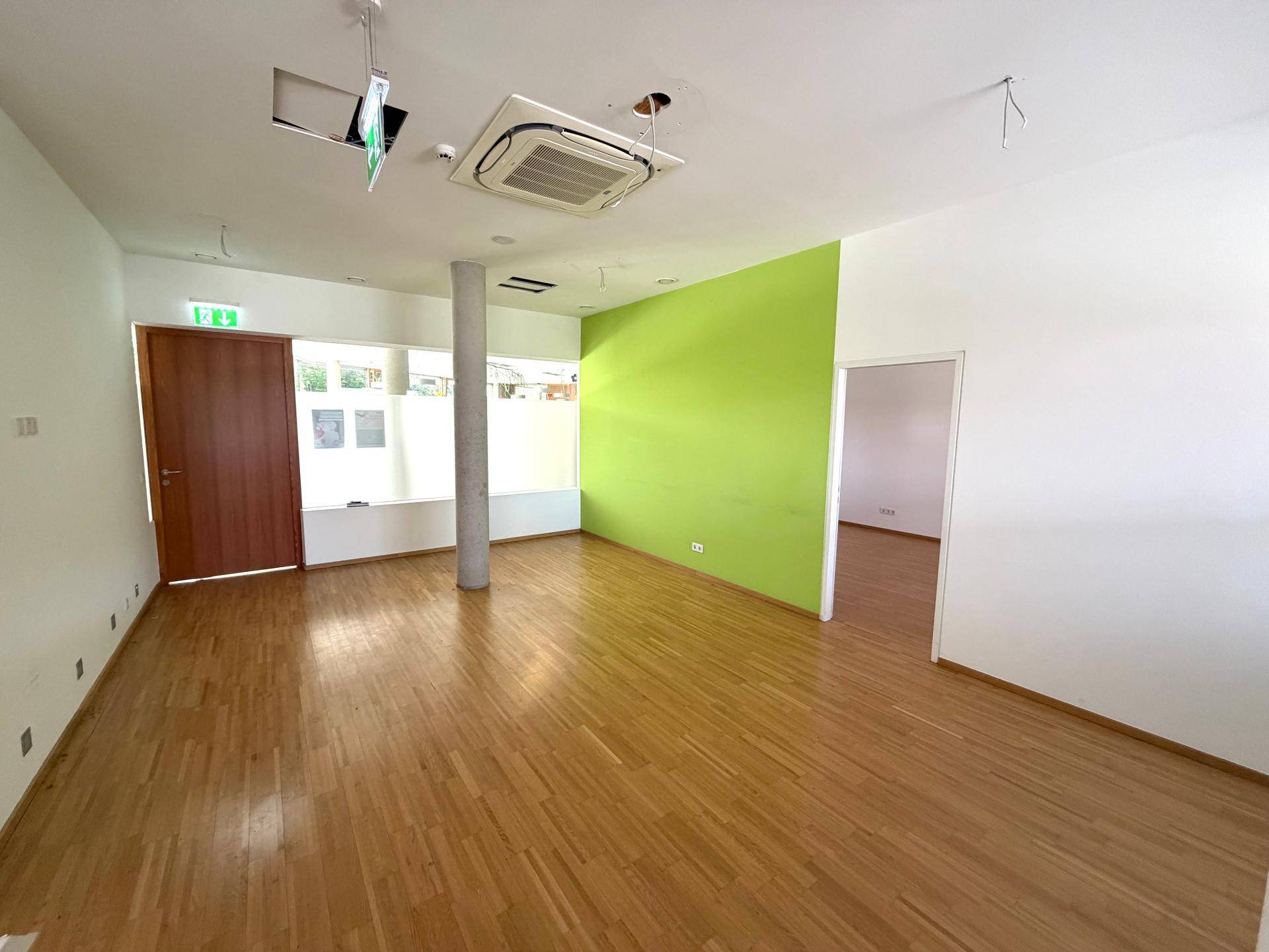 Großzügiger offener Bürobereich mit Holzfußboden, grüner Akzentwand und großen Fenstern.