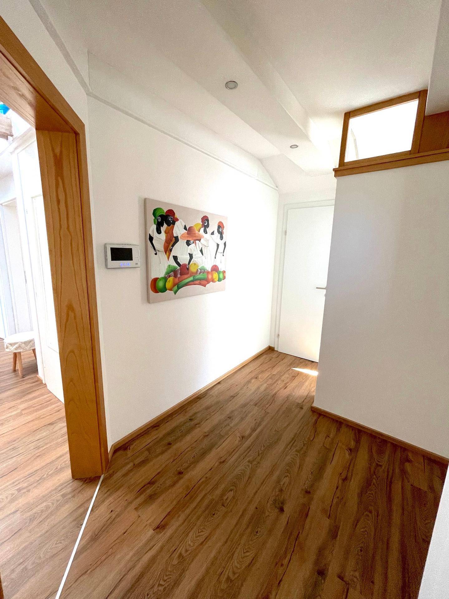 Heller Flur mit Holzboden und moderner Kunst, der zu weiteren Räumen führt.