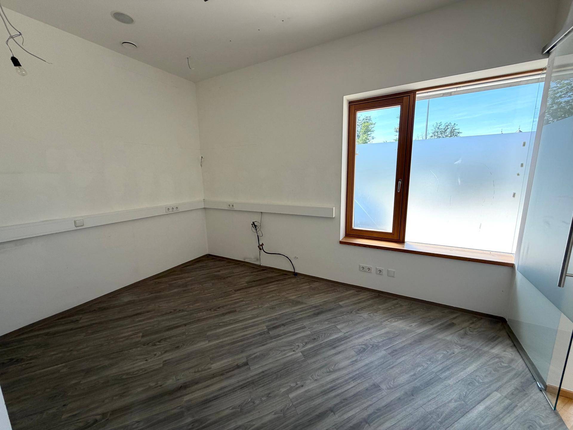 Heller Büroraum mit grauem Laminatboden, weißen Wänden und großen Fenstern.