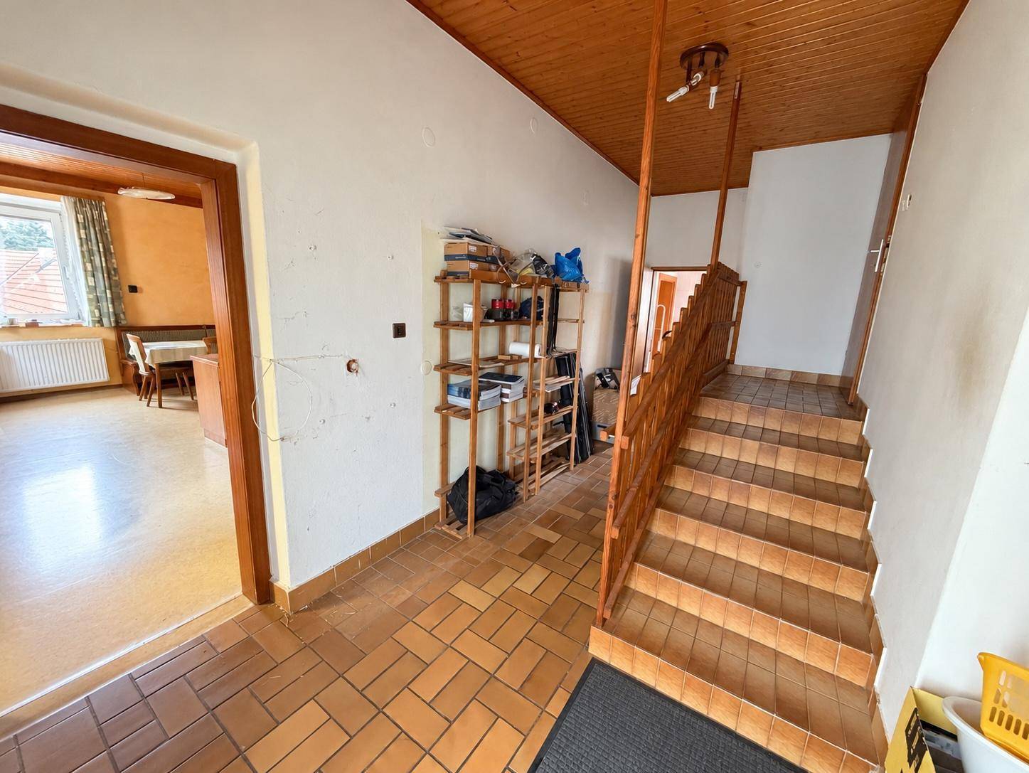 Flur mit Holztreppe, Terrakottafliesen und Stauraum unter der Holzdecke.