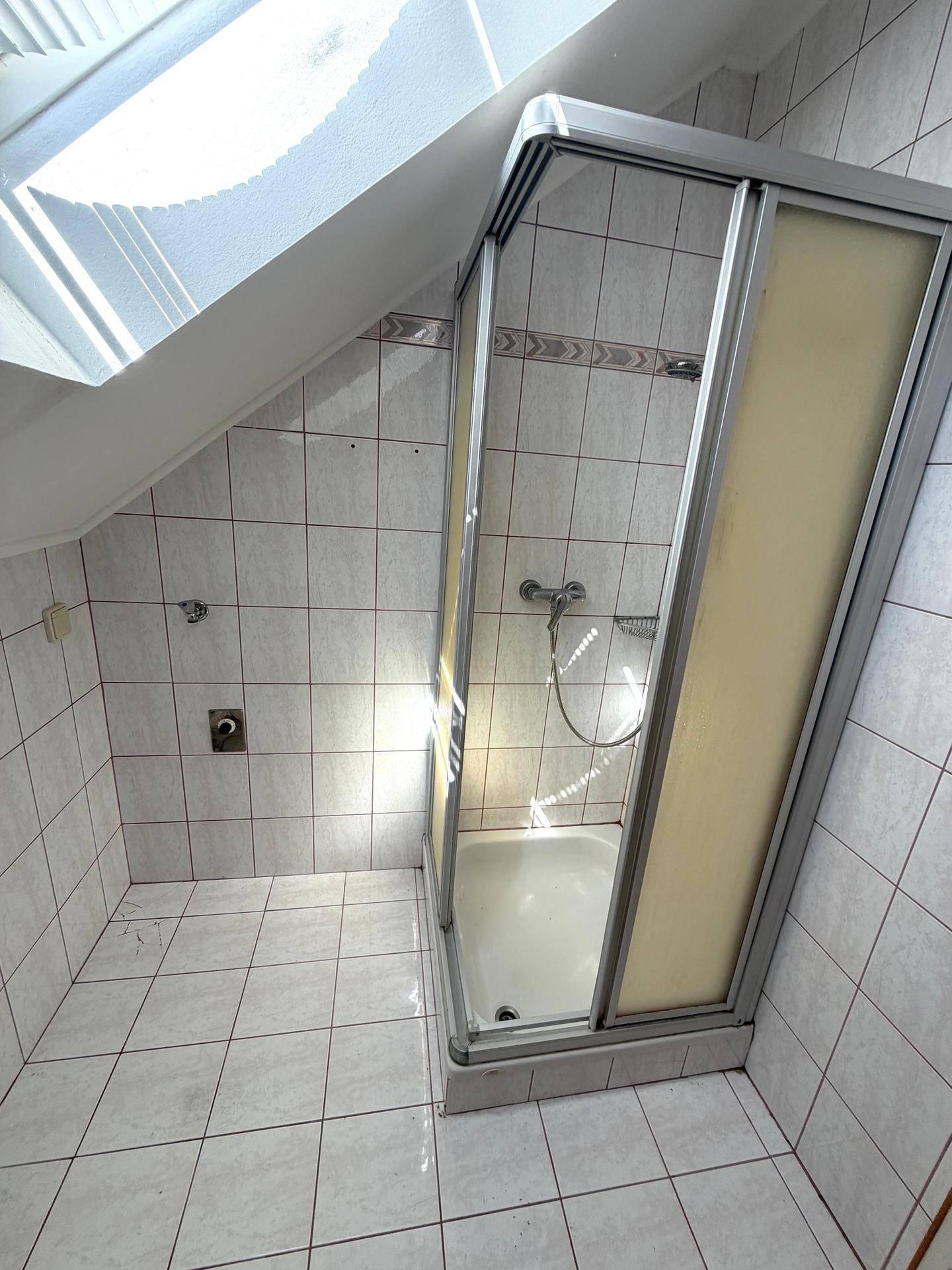 Helles Badezimmer mit Duschkabine, Fliesenboden und natürlichem Licht durch das Dachfenster.