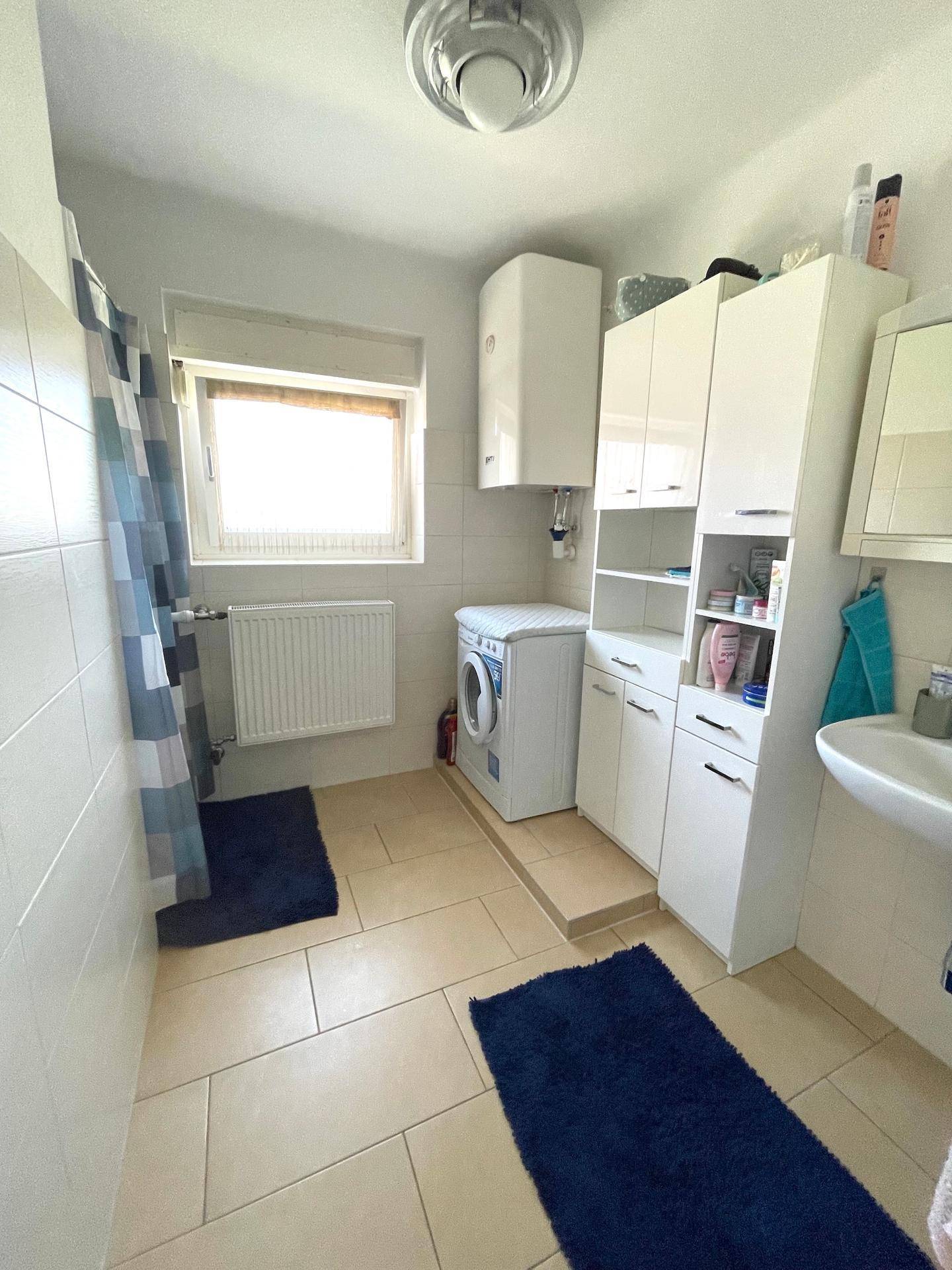 Geräumiges Badezimmer mit Dusche, Waschmaschine und Fenster.