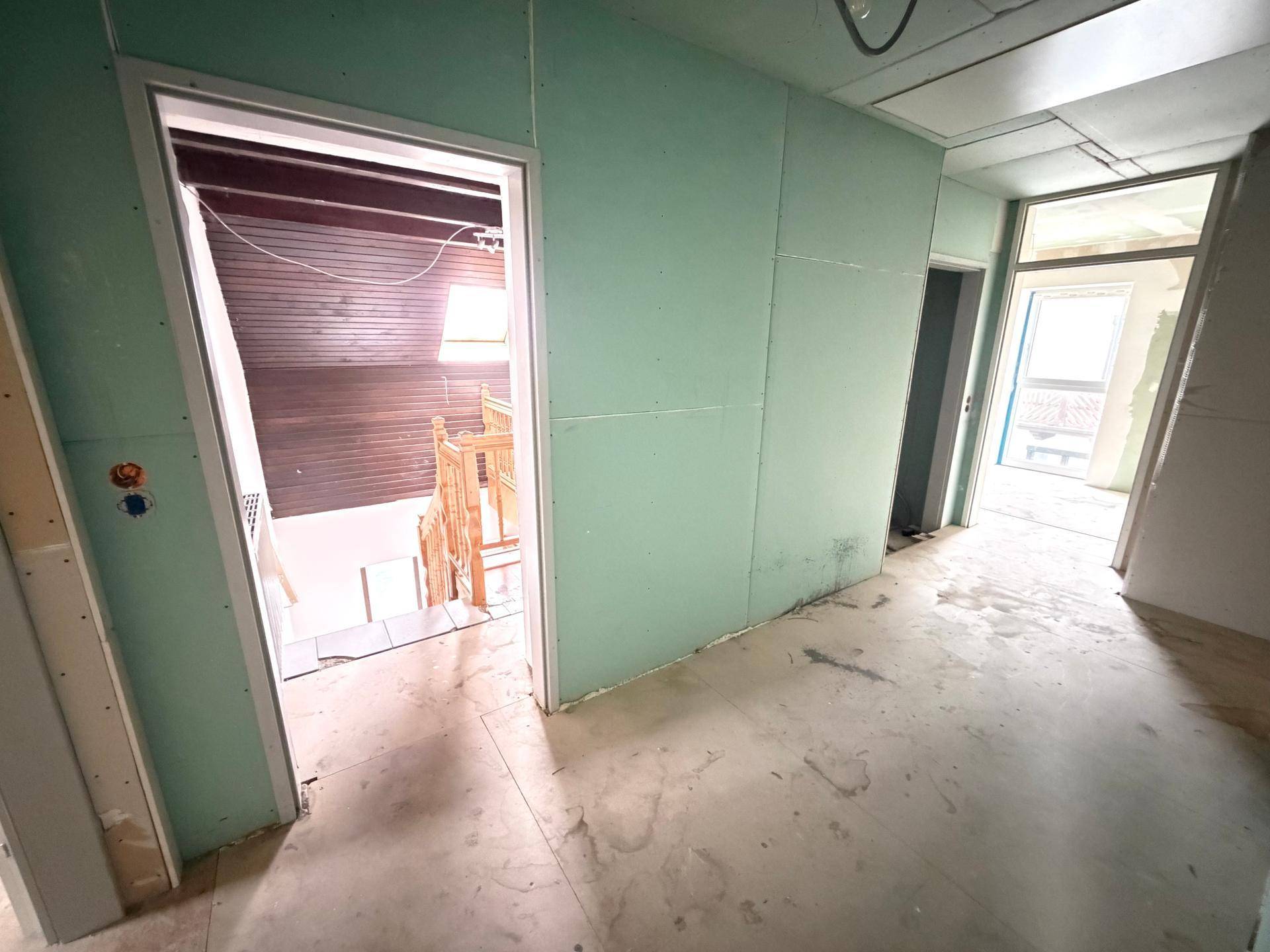 Flur im Rohbau mit Gipskartonwänden und unfertigem Boden, führt zu weiteren Räumen im Ausbau.