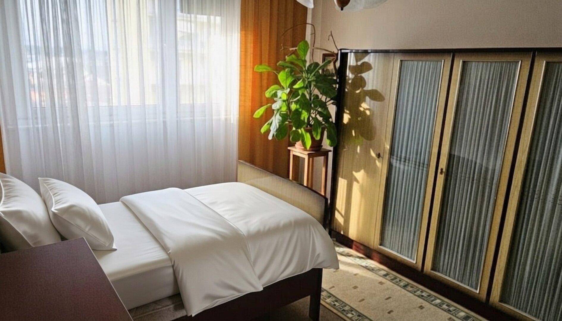 Sonnenverwöhntes Schlafzimmer mit Einzelbett, großem Fenster und einem Kleiderschrank.