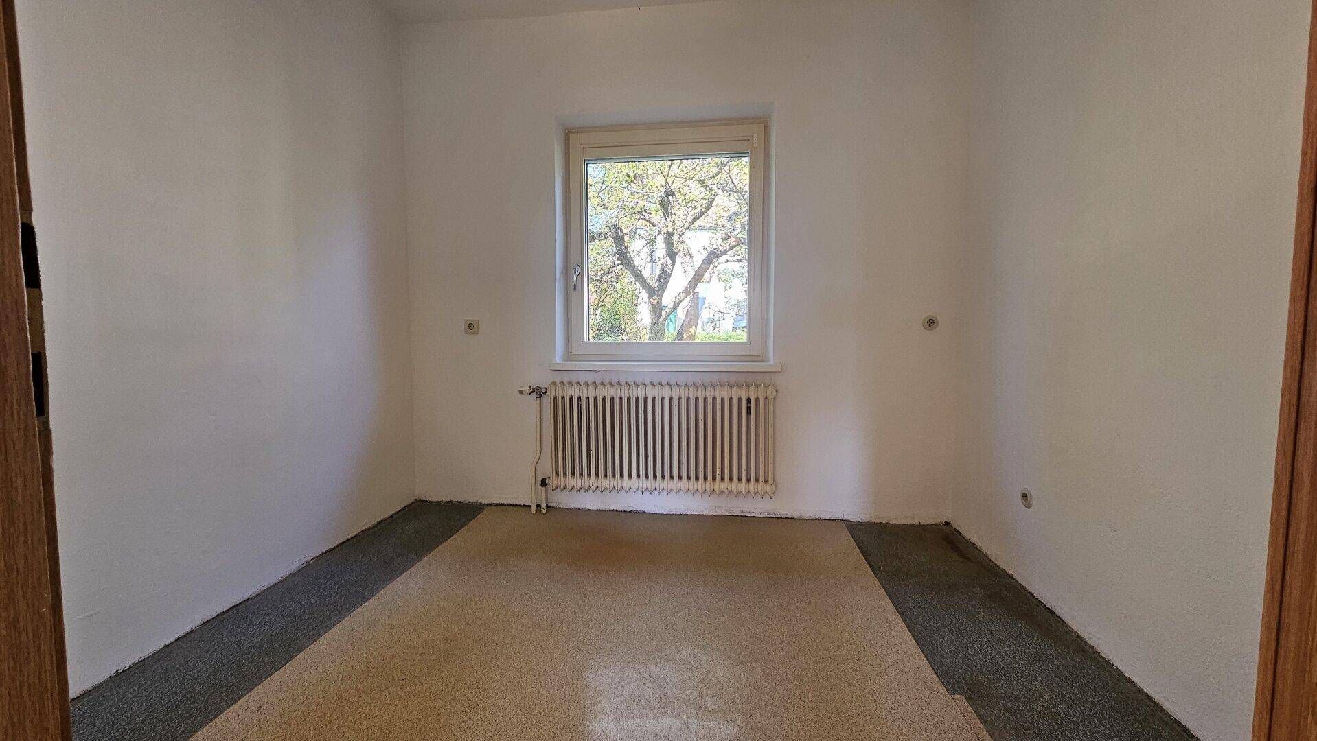 Gemütliches Schlafzimmer mit Teppichboden, Fenster und Heizkörper, bereit zur Einrichtung.