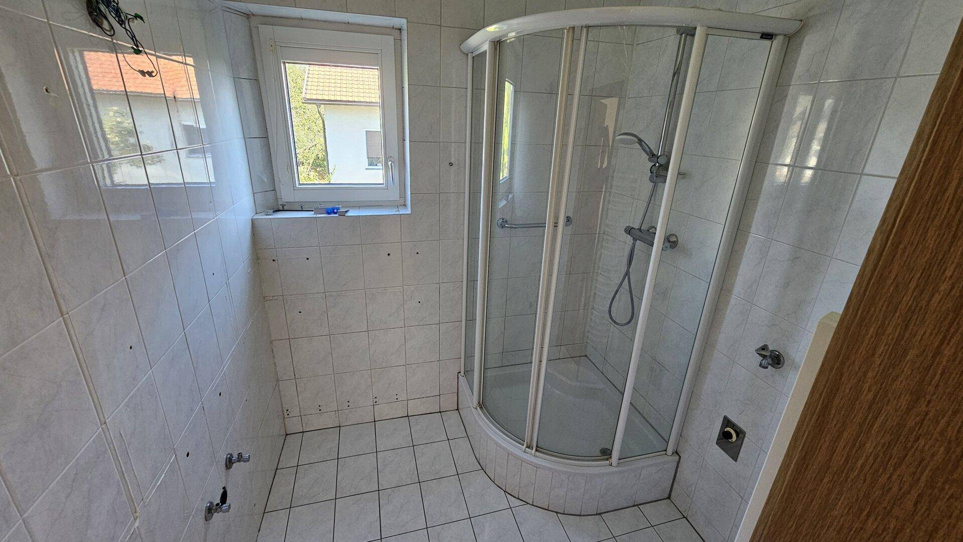 Badezimmer mit weißen Fliesen, Eckduschkabine und Fenster für natürliche Belüftung.