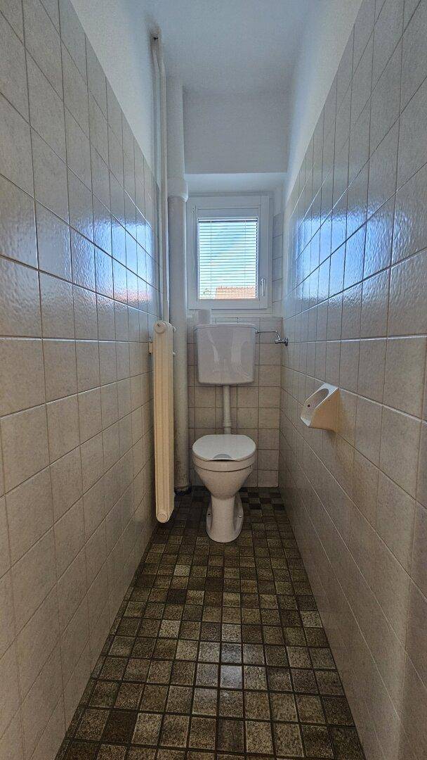 Separates WC mit gefliestem Boden und Wänden, Toilette und kleinem Fenster.