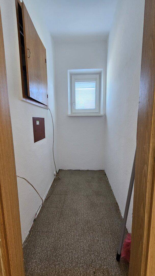 Kleiner Abstellraum mit Teppichboden, Fenster und praktischem Wandschrank.
