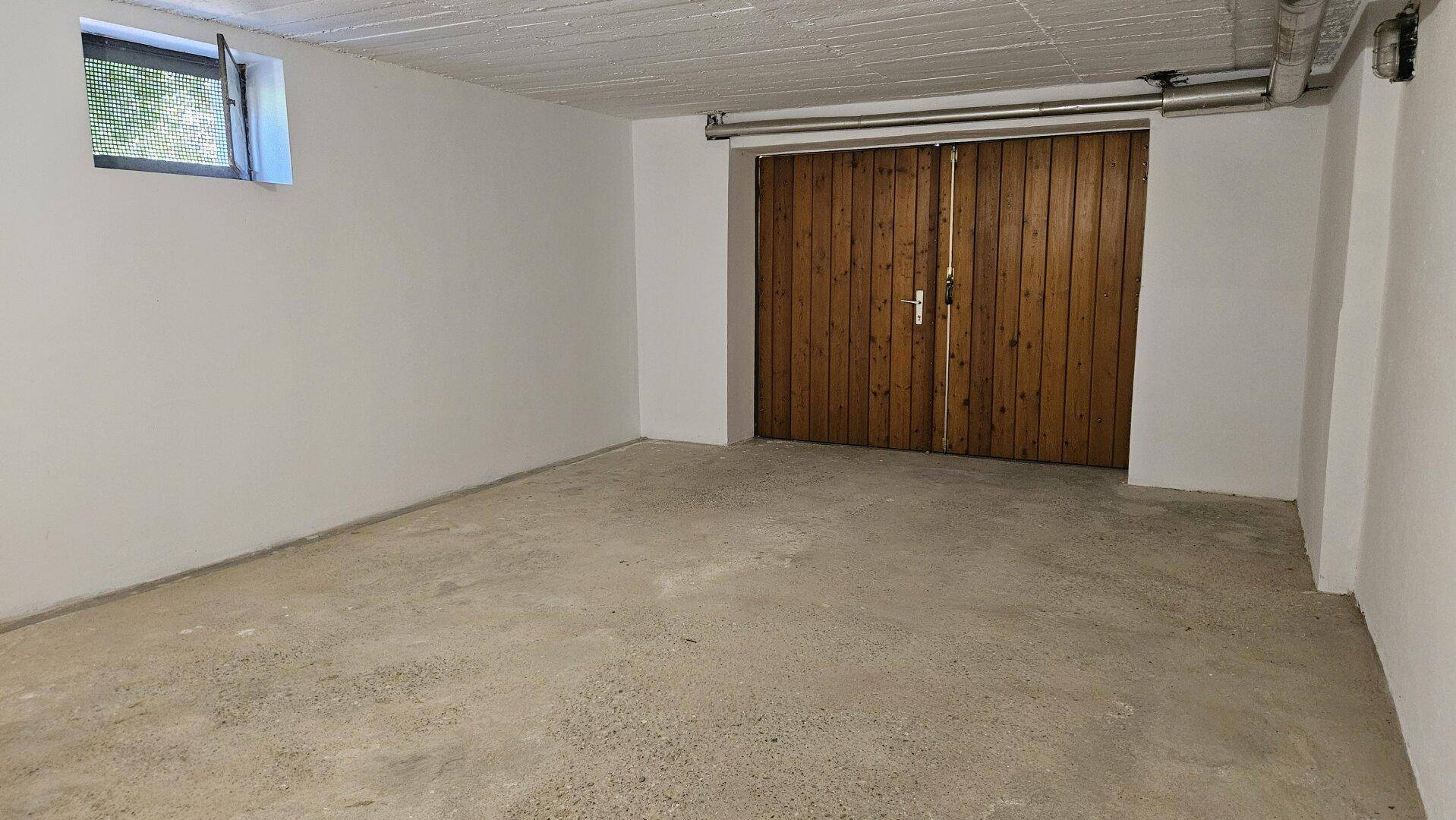 Großer Garagenraum im Untergeschoss mit Betonboden und breiten Holztoren.