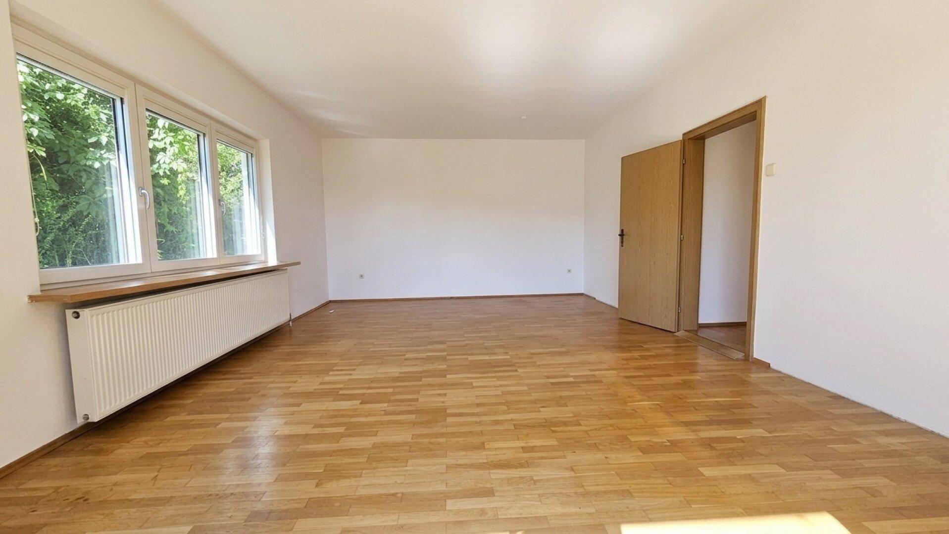 Heller Raum mit Parkettboden, Fenster und zwei Holztüren, bereit zur individuellen Gestaltung.