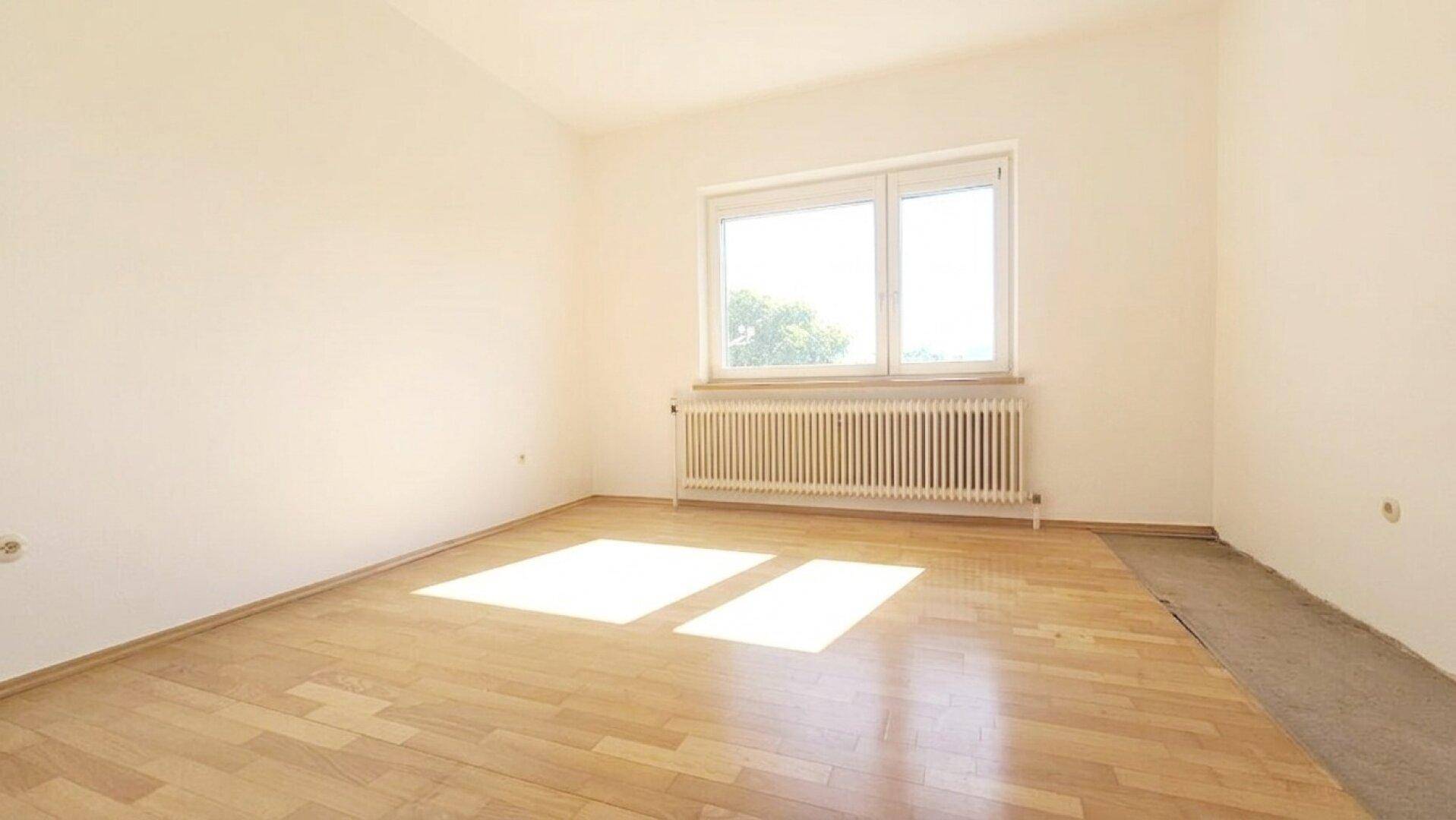 Sonniger Raum mit Parkettboden, Fenster und Heizkörper, ideal als Schlaf- oder Kinderzimmer.