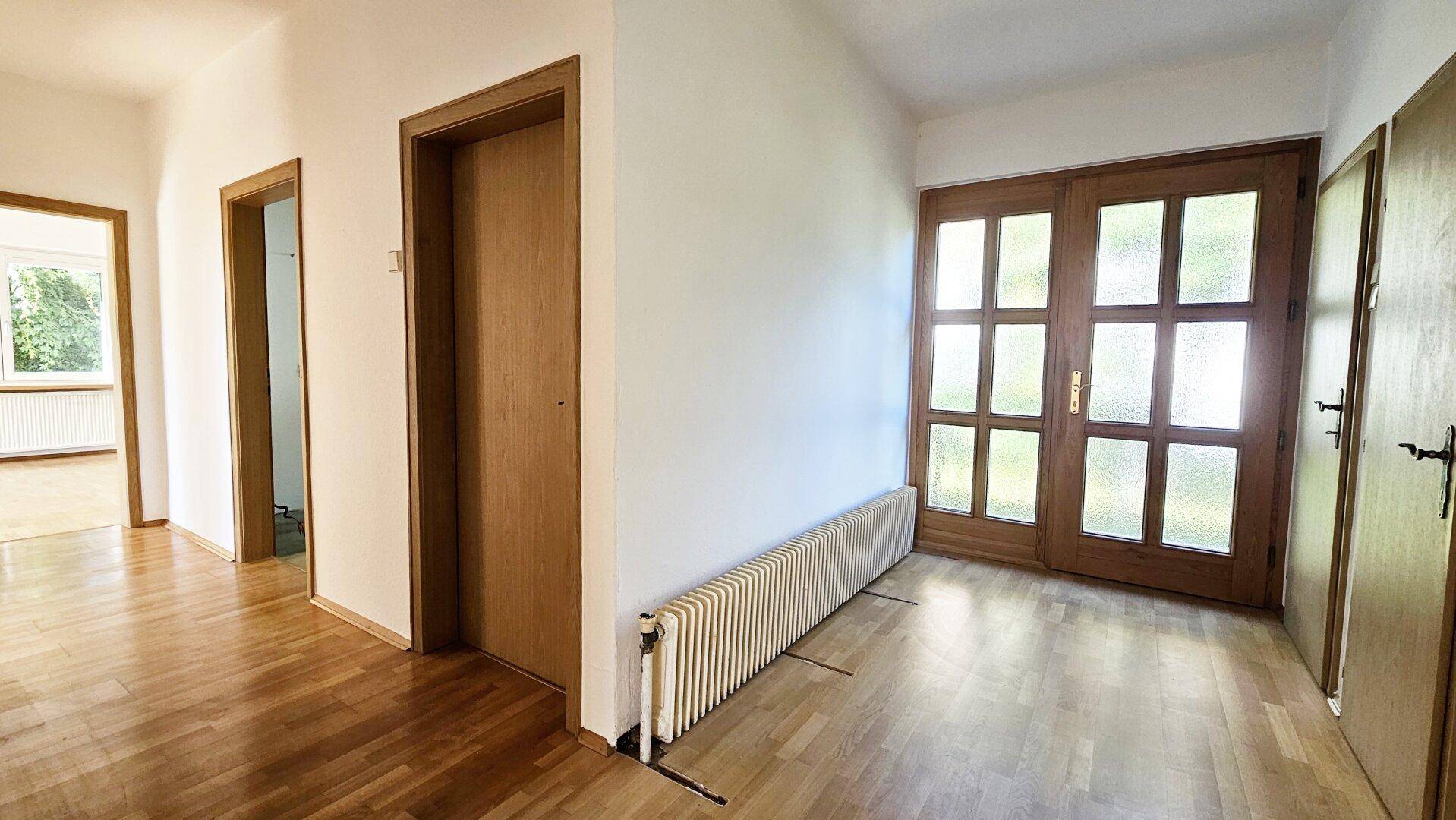 Heller Flur mit Parkettboden, Holztüren und einer verglasten Doppeltür am Ende.