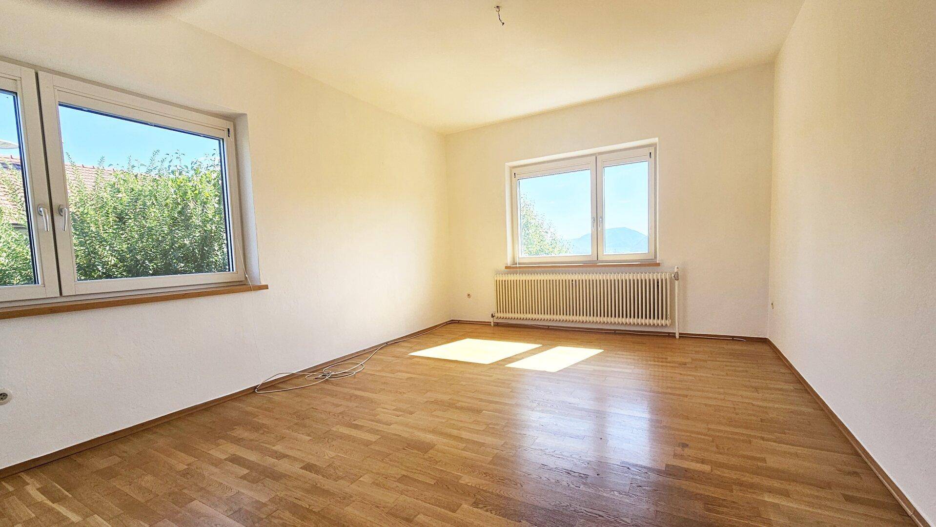 Helles Schlafzimmer mit Parkettboden, zwei Fenstern und viel natürlichem Lichteinfall.