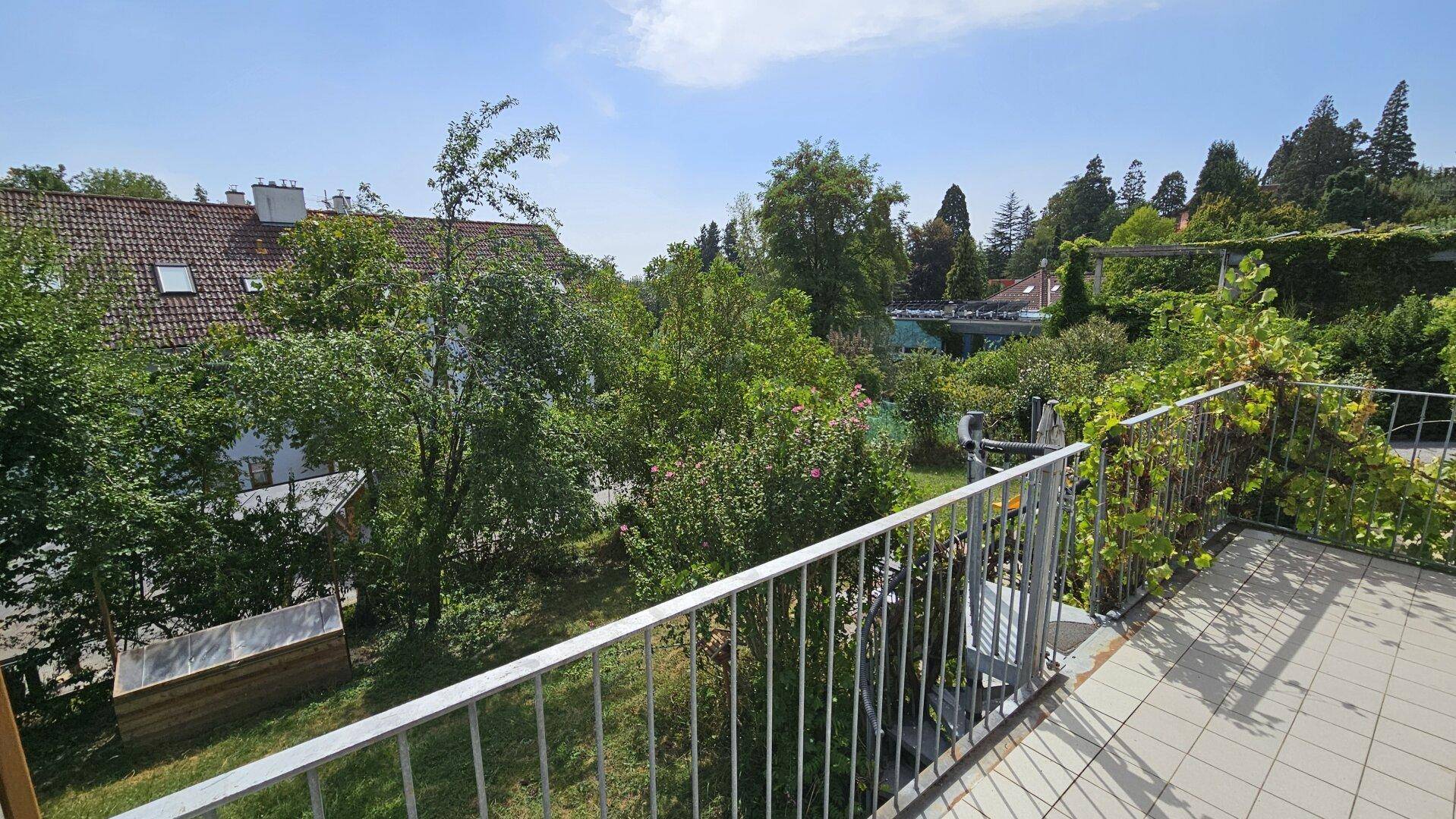 Geräumiger Balkon mit Fliesenboden und weitem Blick über grüne Gärten und Dächer.