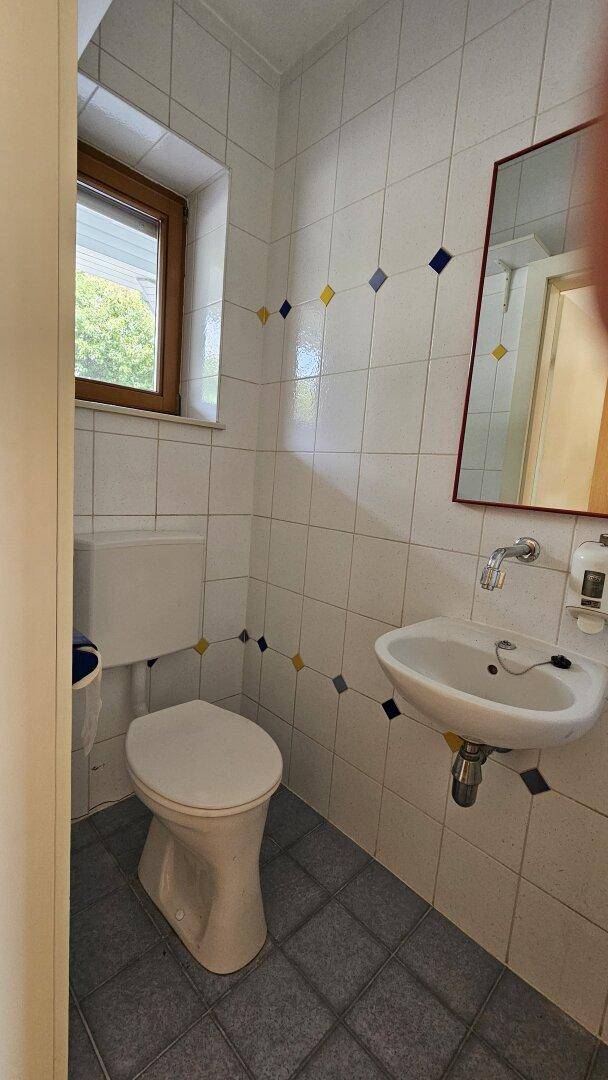 Gäste-WC mit weißen Fliesen, Fenster und einem Waschbecken mit Spiegel.